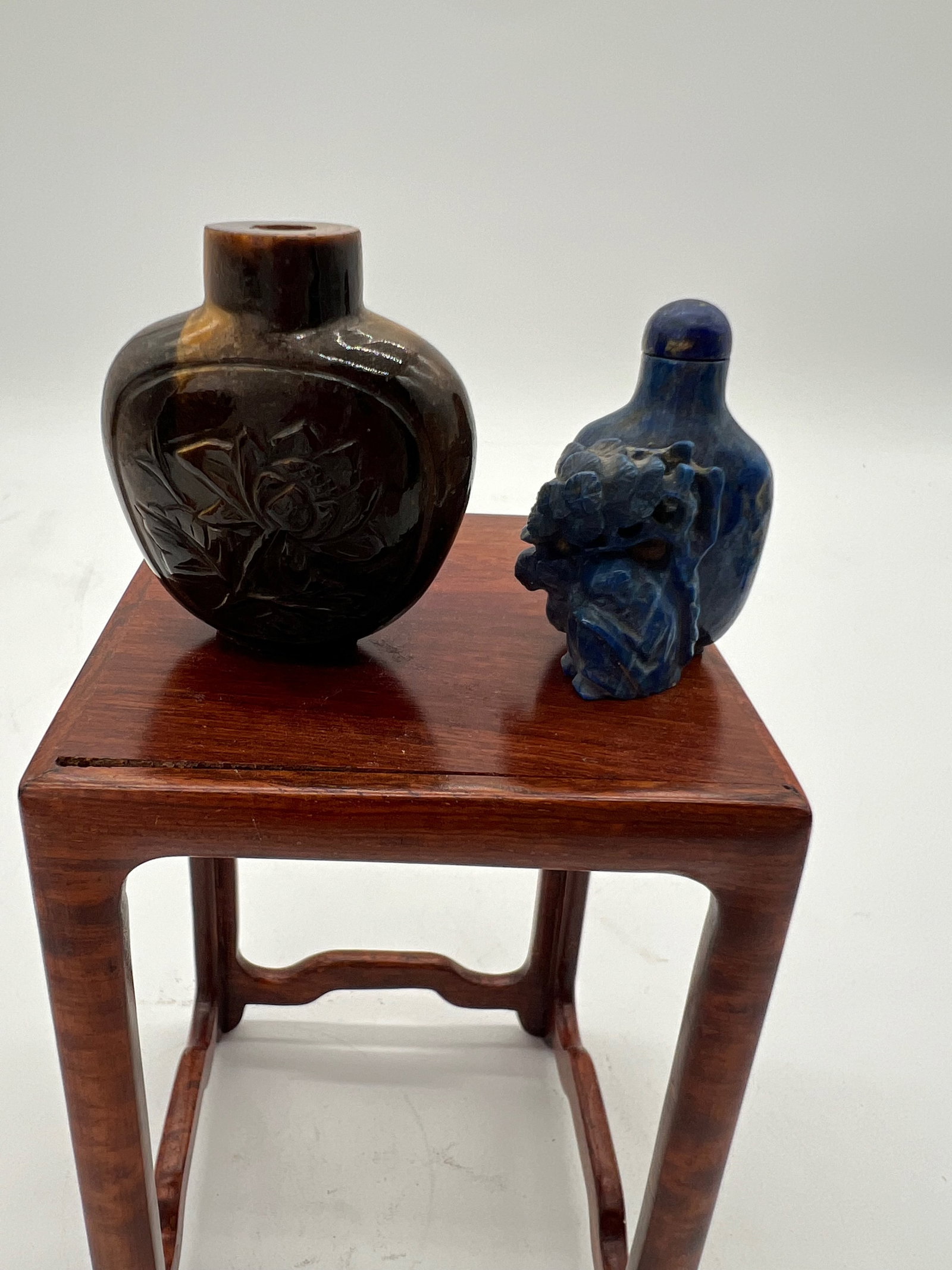 A Chinese tiger eye snuff bottle and a Chinese lapis snuff bottle: Qing Dynasty (1644–1912) ; Hand carved from lapis given the rich, deep blue tones with natural veining. Intricate carving with a sculptural or figural design, possibly depicting a natural or mythica