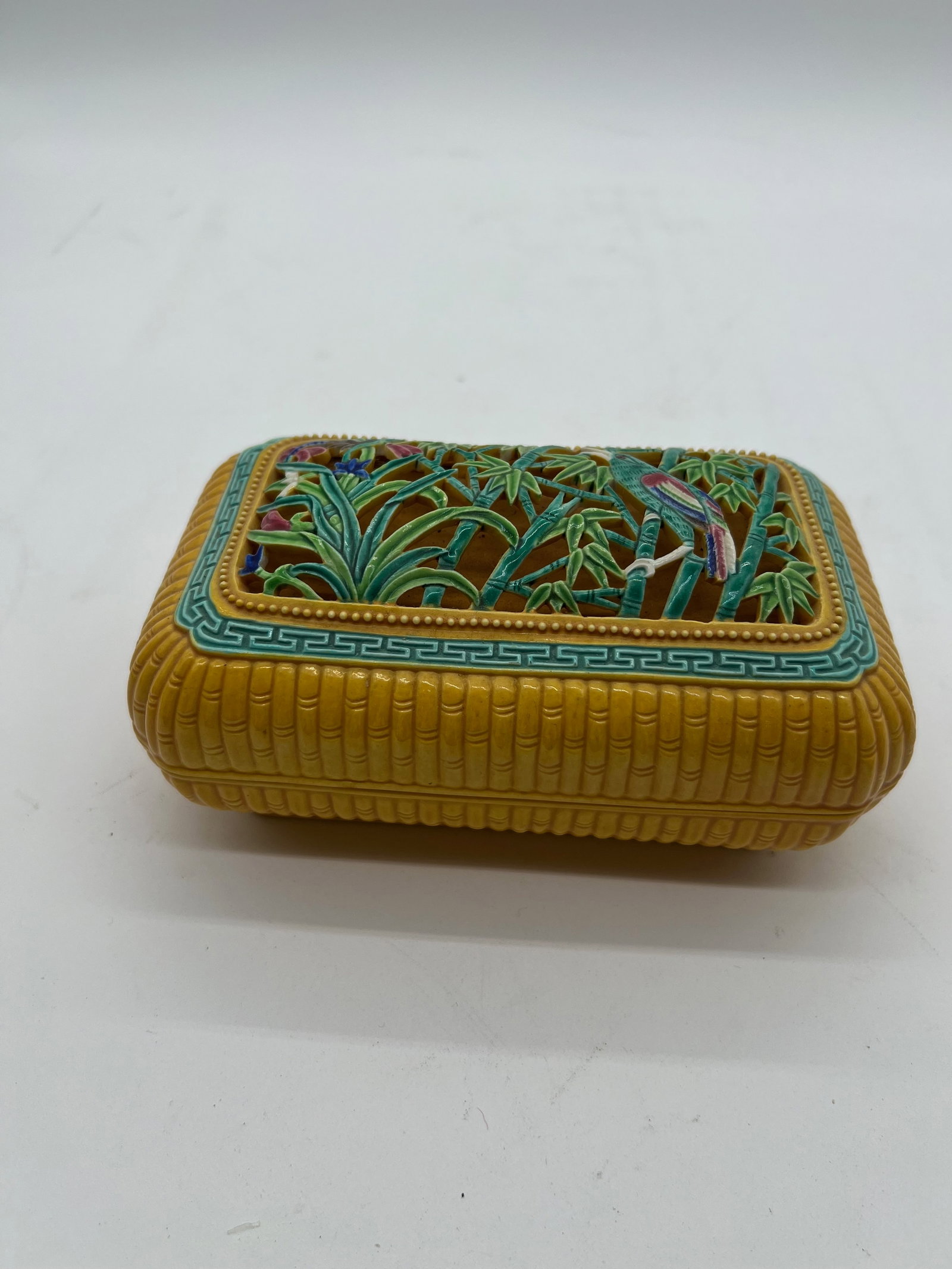 A Chinese yellow glazed porcelain box with QianLong carved Mark: Qing dynasty (1644-1912); The lid features a colorful relief pattern of bamboo and a bird, possibly a parrot or a similar exotic species. The raised design and vibrant colors give the piece a lively, 