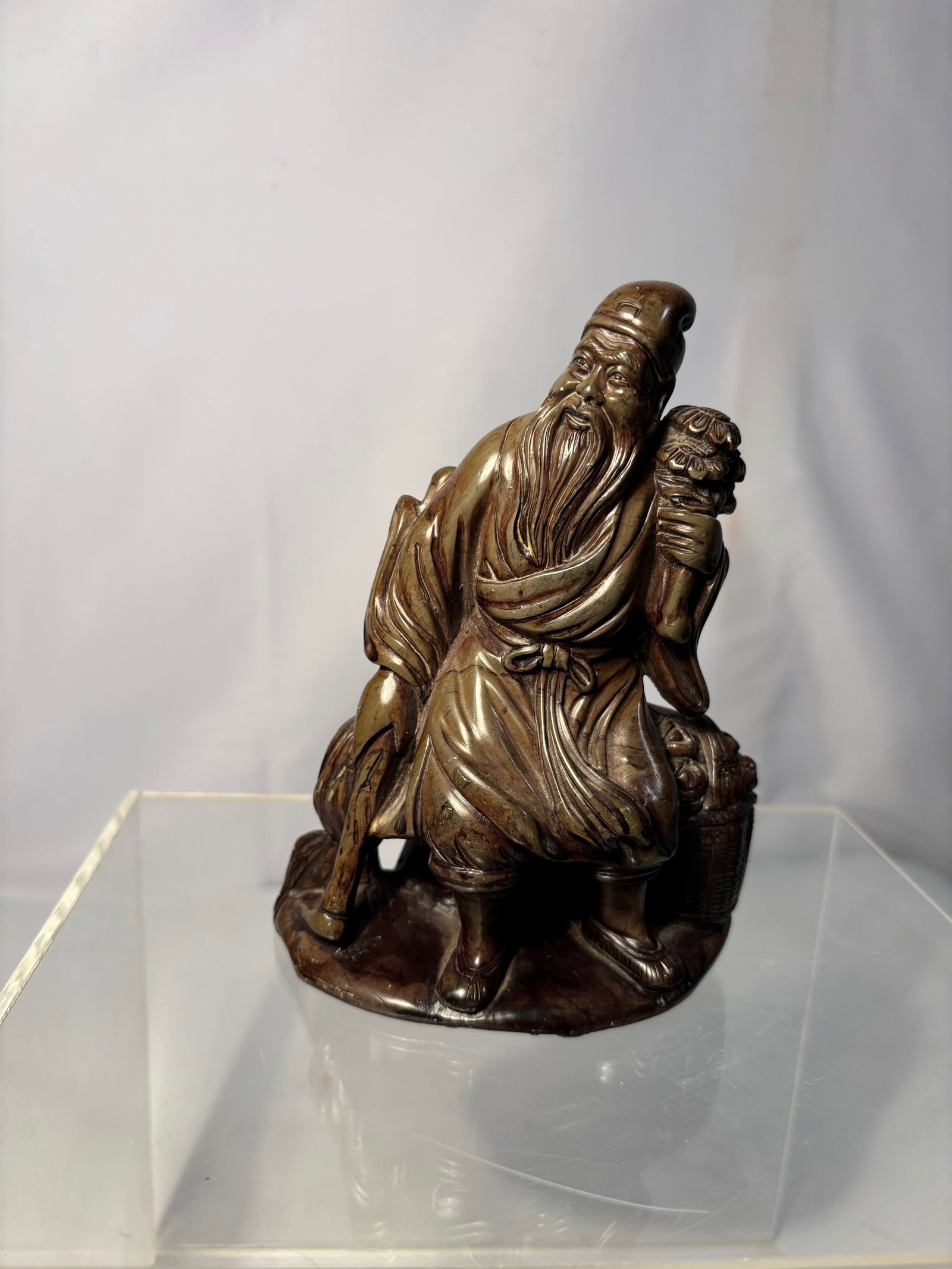 A Chinese Carved Soapstone Figure of Shoulao: Carved soapstone figure depicting Shoulao, the God of Longevity, shown standing in flowing robes and holding a staff with a gourd finial. The figure features detailed facial expression, long flowing b
