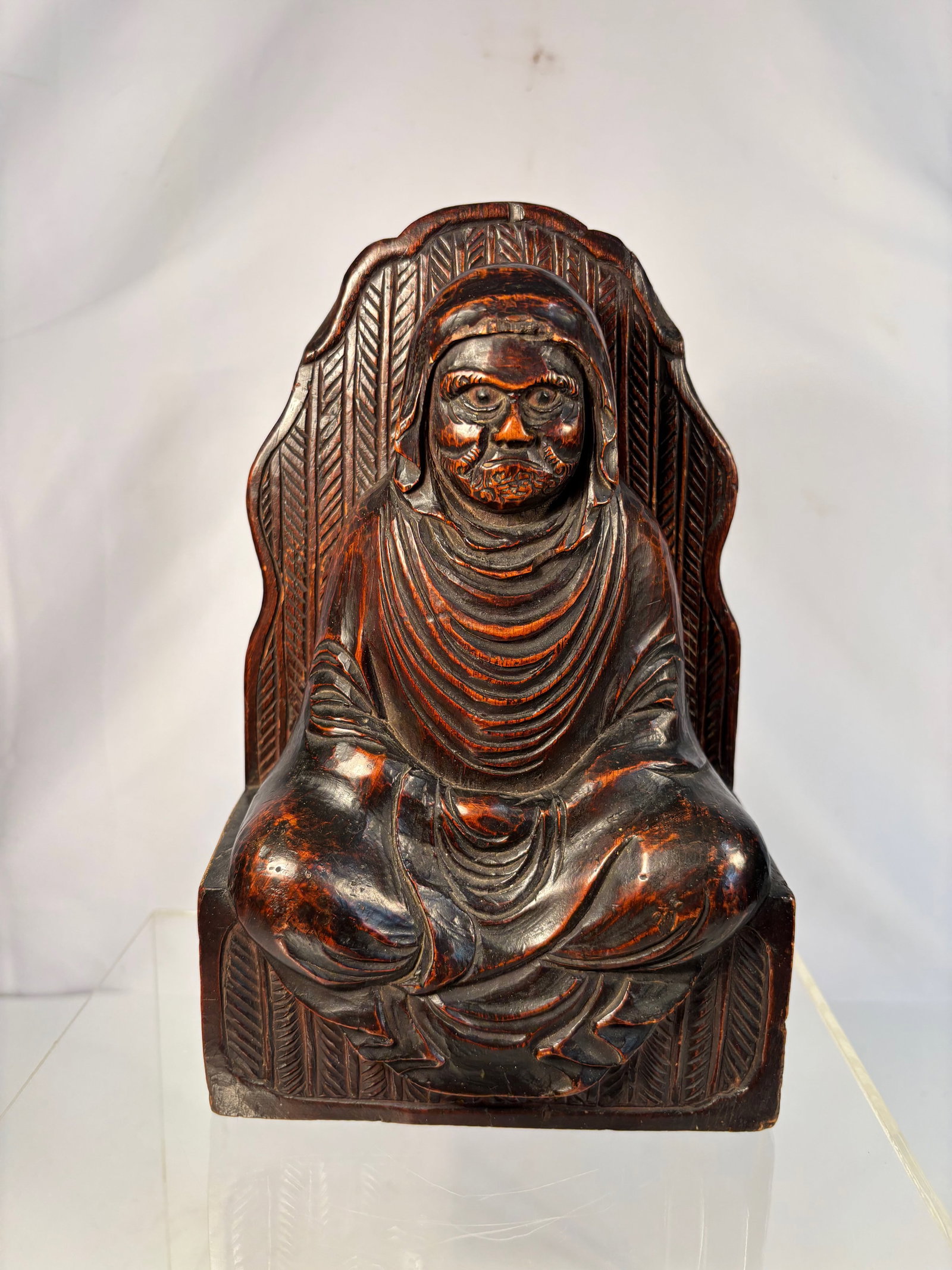 A Japanese Carved Wood Figure of Daruma (Bodhidharma), Meiji–Taish? Period (Late 19th–Early: Finely carved seated figure of Daruma, the founder of Zen Buddhism, depicted with intense expression and deeply incised drapery folds, his robe cascading in naturalistic folds across his body. The fig