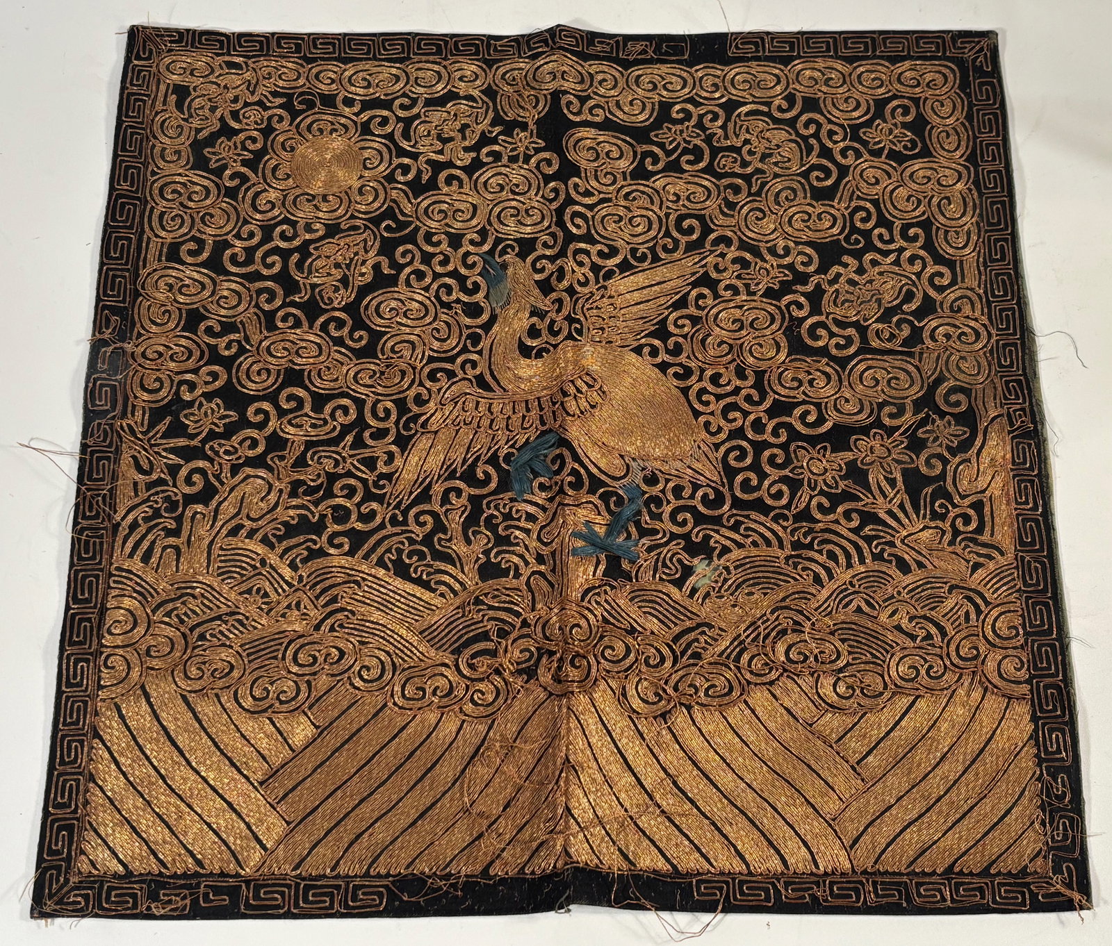 A Chinese Embroidered Civil Rank Badge with First-Rank Crane: Qing dynasty(1644-1912) ; A Chinese embroidered civil rank badge (buzi) depicting the first-rank crane (xianhe) standing on a rocky outcrop above stylized waves, surrounded by dense gold-thread cloud 