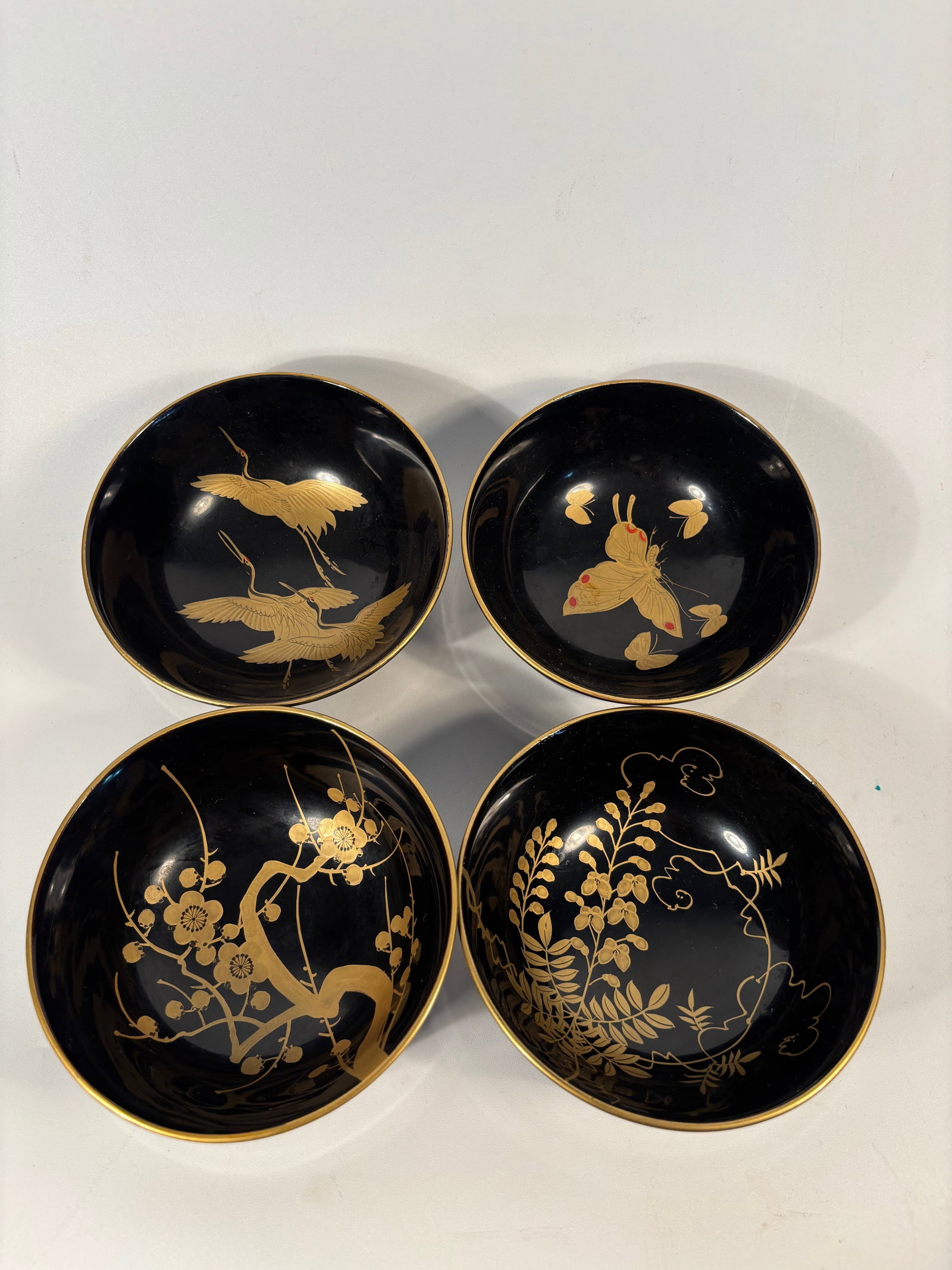 Set of 4 Japanese Makie Lacquer Bowls: Each bowl finely decorated in gold maki-e on black lacquer with traditional Japanese motifs including plum blossoms, cranes in flight, butterflies, and flowering vines. The designs are delicately rend