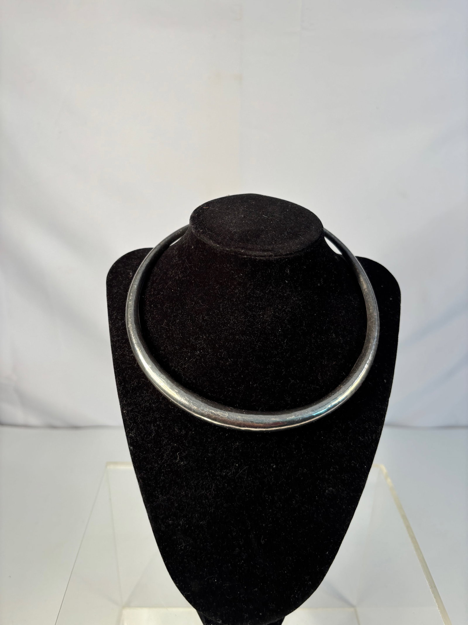 A Silver Torque-Style Collar Necklace: A rigid silver neck ring designed in the traditional torque form, with open ends capped by small rounded finials. The smooth, polished surface shows natural patina consistent with age. Dimensions?Inne