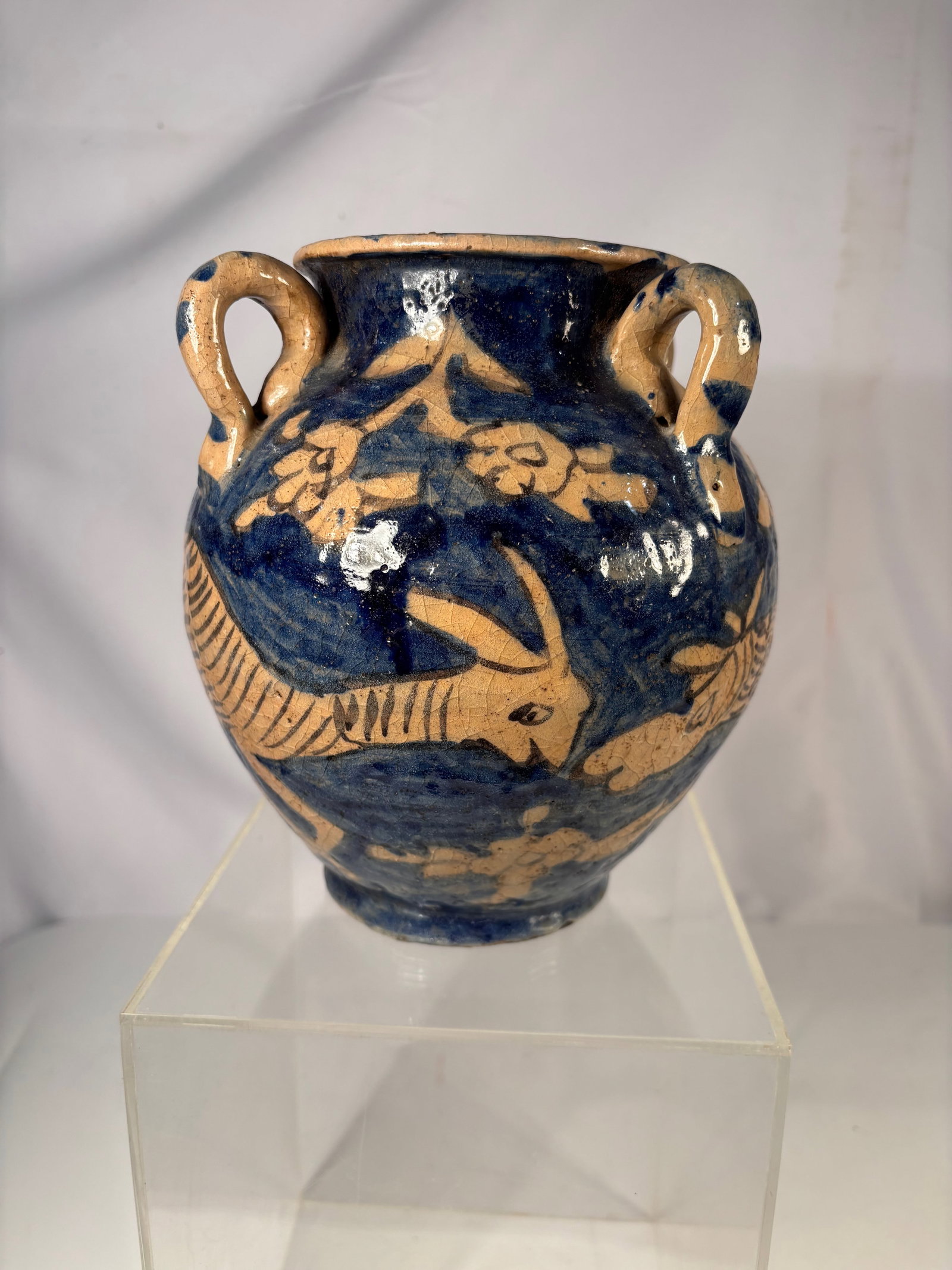 A Spanish Folk Pottery Earthenware Jar with Cobalt Fish Decoration 19th century: A hand-thrown earthenware vessel decorated with cobalt blue glaze depicting stylized fish and foliage motifs. The jar features two applied loop handles and a rounded body on a small foot. The interior