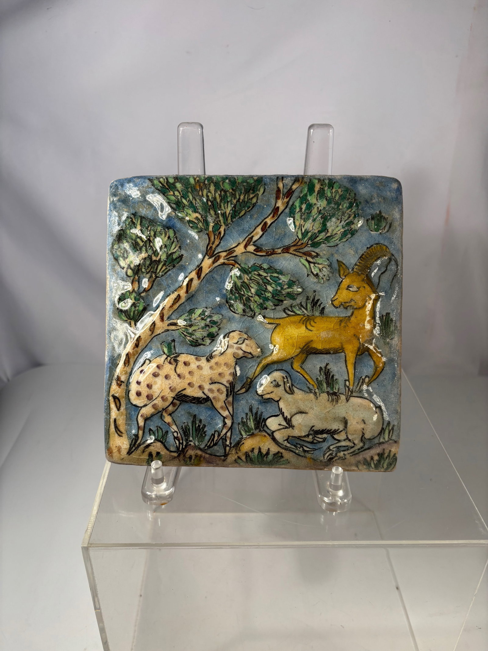 A Persian Qajar Polychrome Glazed Ceramic Tile with Deer and Hounds, 19th C.: A Persian Qajar period polychrome glazed ceramic tile depicting a mounted falconer holding a bird of prey, accompanied by a hunting dog below. The figure is rendered against a turquoise blue ground in