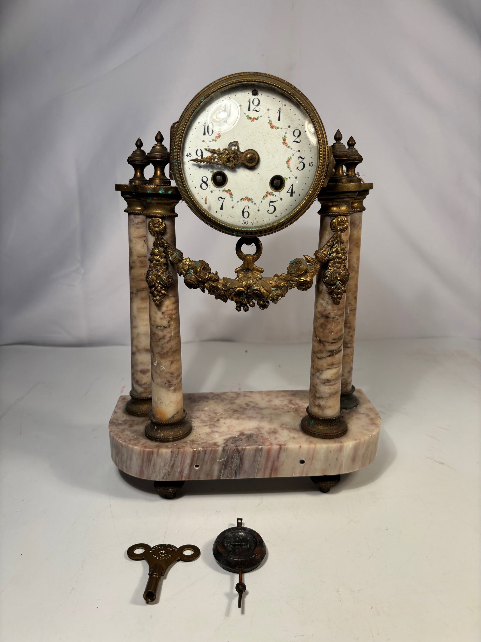 A French Louis XVI Style Marble and Gilt Bronze Mantel Clock, 19th century: Antique French Louis XVI style mantel clock, featuring a white enamel dial with Arabic numerals, floral swag decoration, and ornate gilt bronze hands. The clock is housed in a gilt bronze and marble a