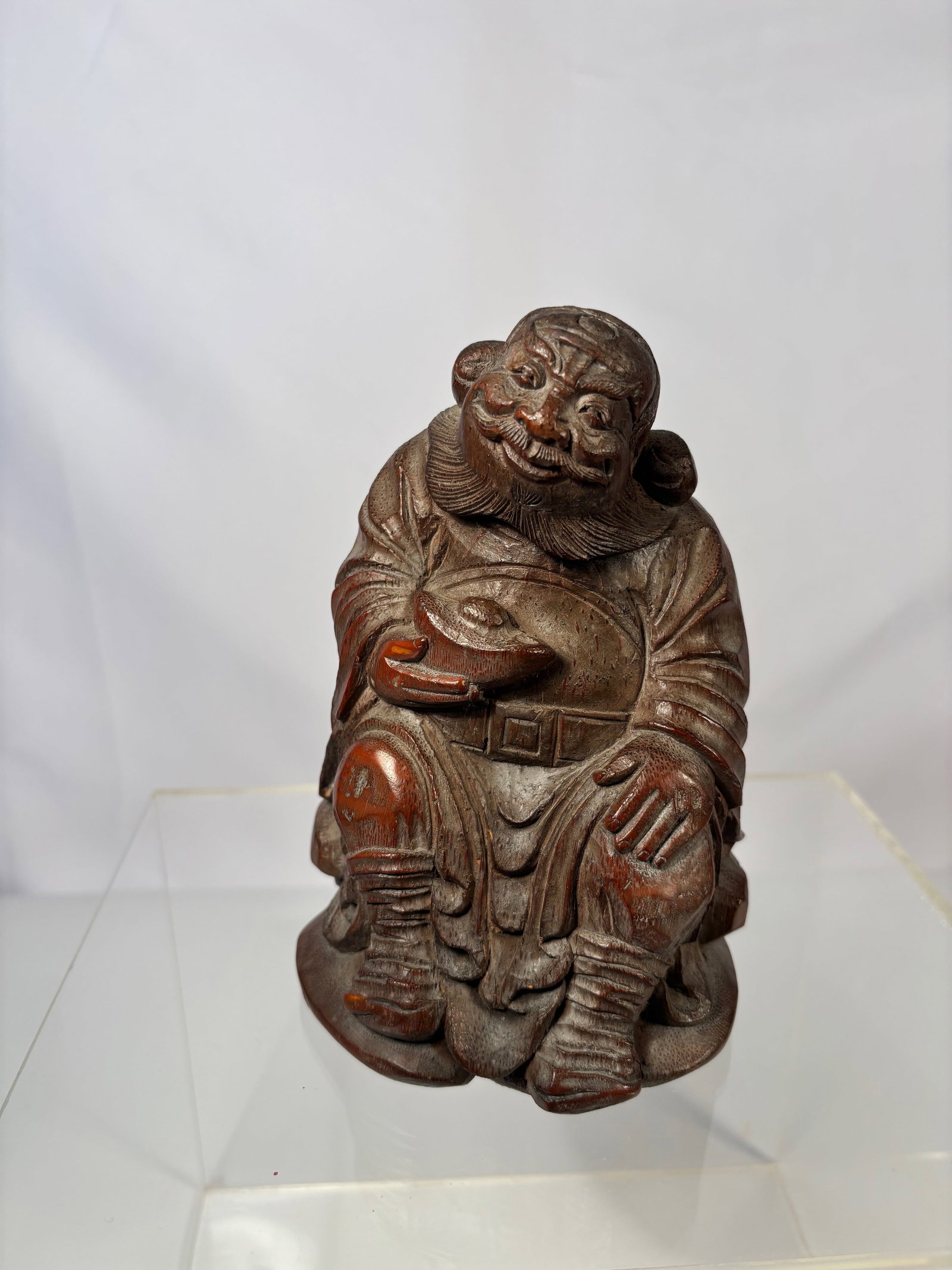 A CHINESE CARVED BAMBOO FIGURE: A well-carved Chinese figure of an immortal, likely fashioned from bamboo root, depicting a smiling elderly man seated in relaxed posture. He holds a wine cup in one hand and wears flowing layered rob