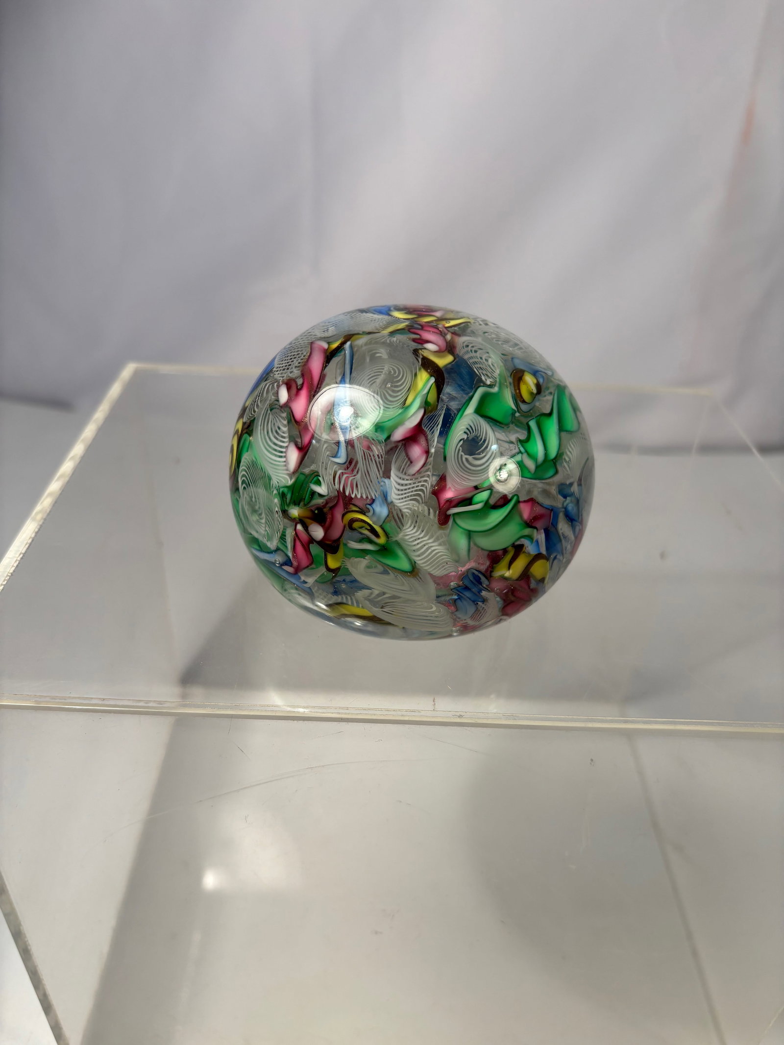 A Large Murano Style Colorful Ribbon Art Glass Paperweight: A colorful Italian Murano style art glass paperweight, featuring vibrant multicolor ribbon inclusion s with fine white latticino decoration suspended within a clear glass dome. The interior displays a