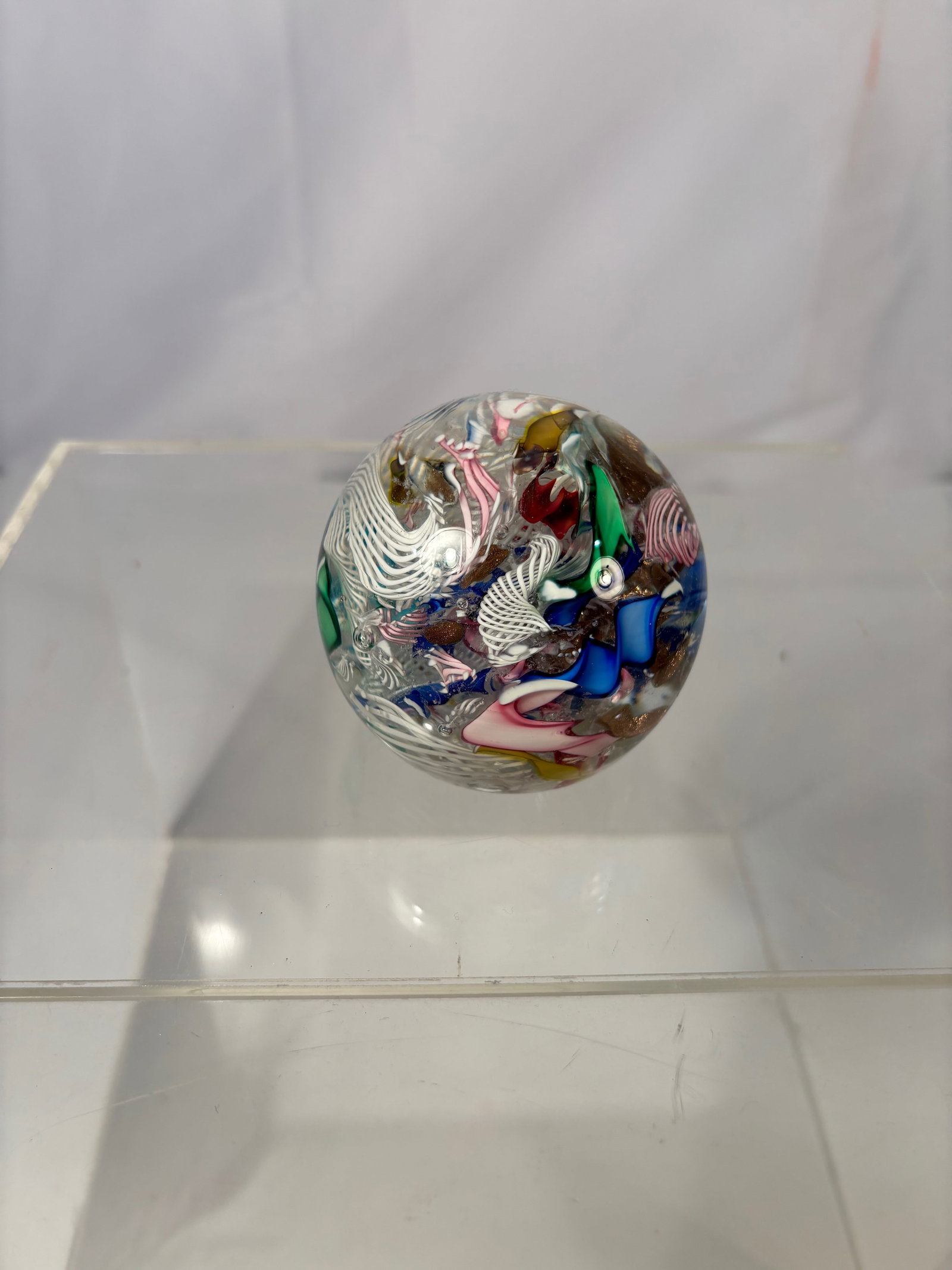 Studio Art Glass Abstract Paperweight with Latticino and Aventurine: Studio art glass paperweight of spherical form, internally decorated with an abstract composition of fused multicolored glass fragments. The design incorporates latticino-style white pulled threads, r