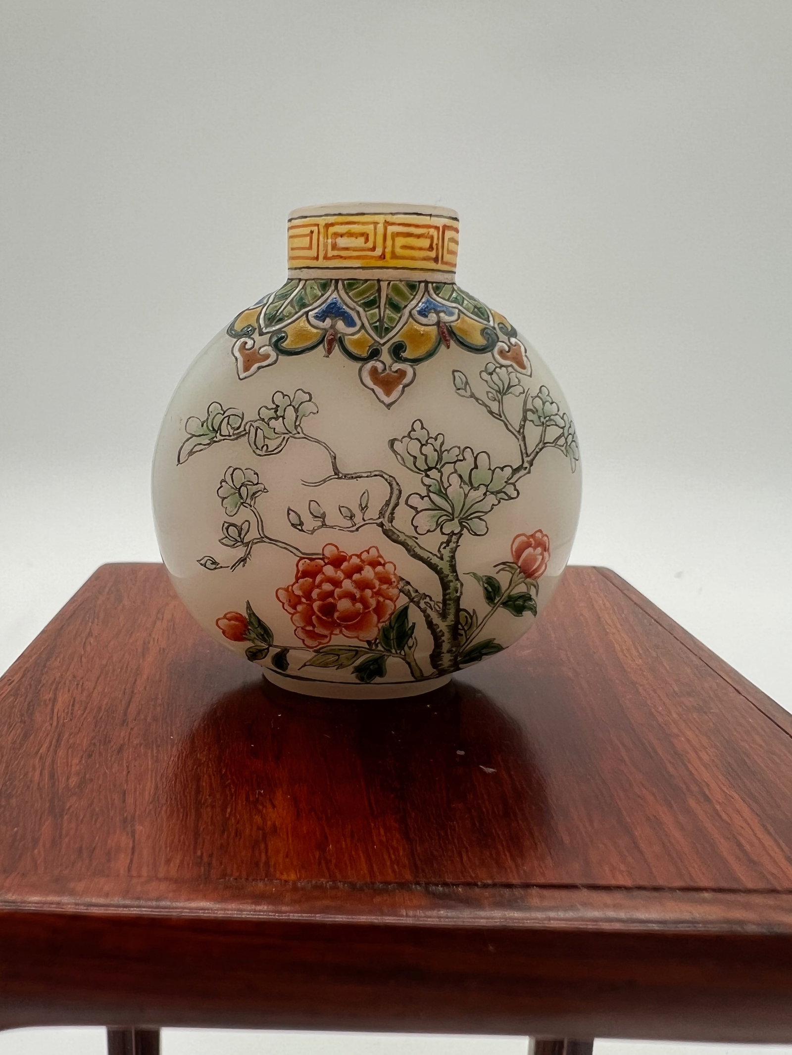 A Chinese white peking glass enameled snuff bottle, with Qianlong Four Characters Mark,: Qing Dynasty (1644-1912); finely enameled with a continuous design of a lush garden setting ,with two birds standing on the tree branch ,the other side with flowering roses motifs .Dimensions?Height: 