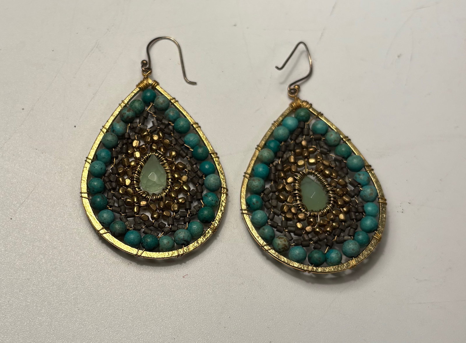 A Pair of Beaded Teardrop Earrings with Turquoise Beads: Pair of handcrafted teardrop-shaped earrings decorated with concentric rows of small turquoise beads surrounding a central pale green stone. The beads are arranged in layered patterns within a metal f