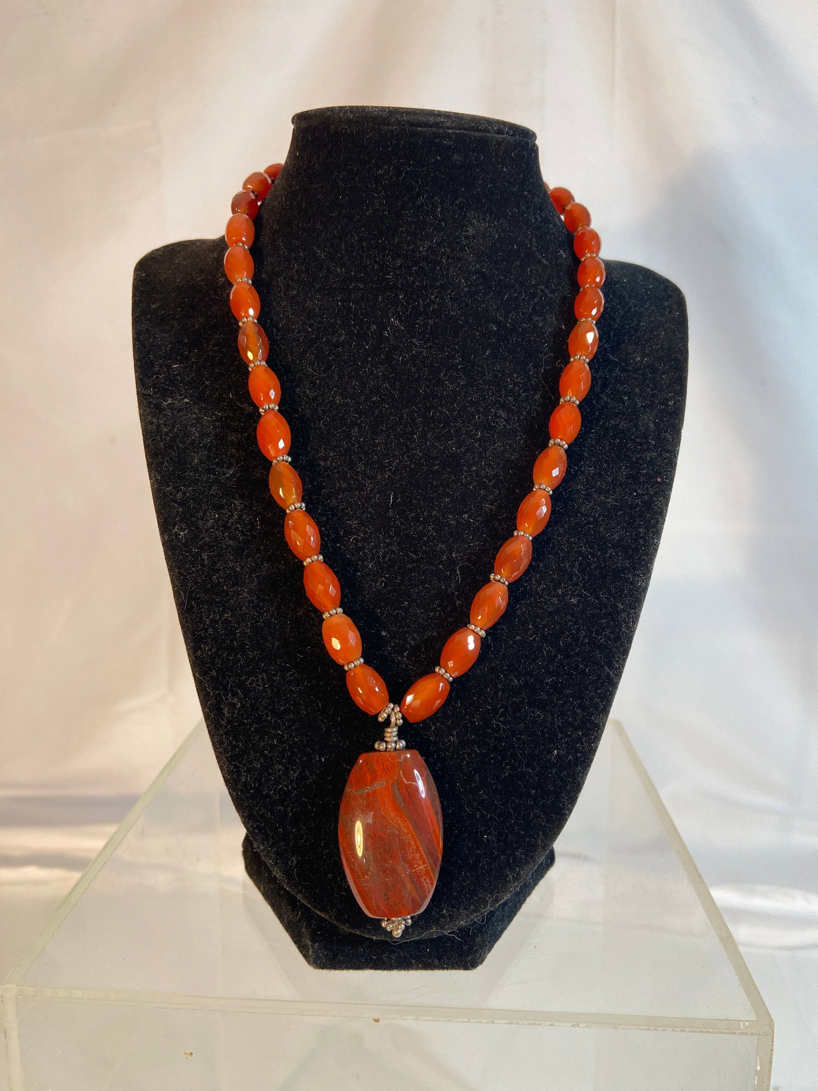 Carnelian and Red Jasper Pendant Necklace: Necklace composed of faceted orange-red carnelian beads accented by silver-tone spacers, centered with a large polished red jasper style pendant displaying natural banded coloration. Artisan style jew