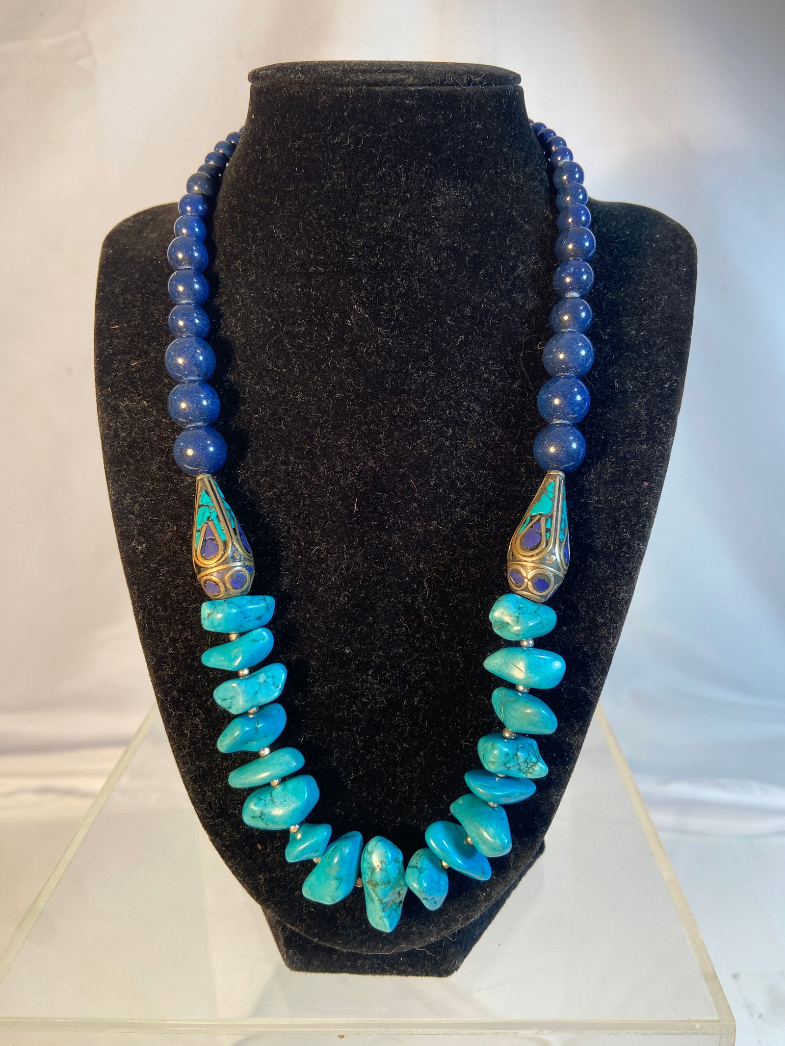 Tibetan Style Lapis and Turquoise Statement Necklace: Bold Tibetan style statement necklace composed of lapis style blue bead strands with turquoise style nugget beads and large decorative inlaid metal focal elements. Featuring brass tone accents and adj