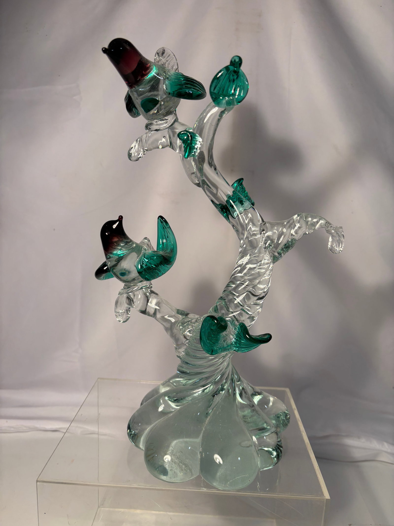 Hand-Blown Art Glass Bird Tree Sculpture: Decorative hand-blown art glass sculpture depicting colorful birds perched upon a clear twisted tree branch with applied green leaves. Raised on an organic clear glass base. Executed in the Murano tas