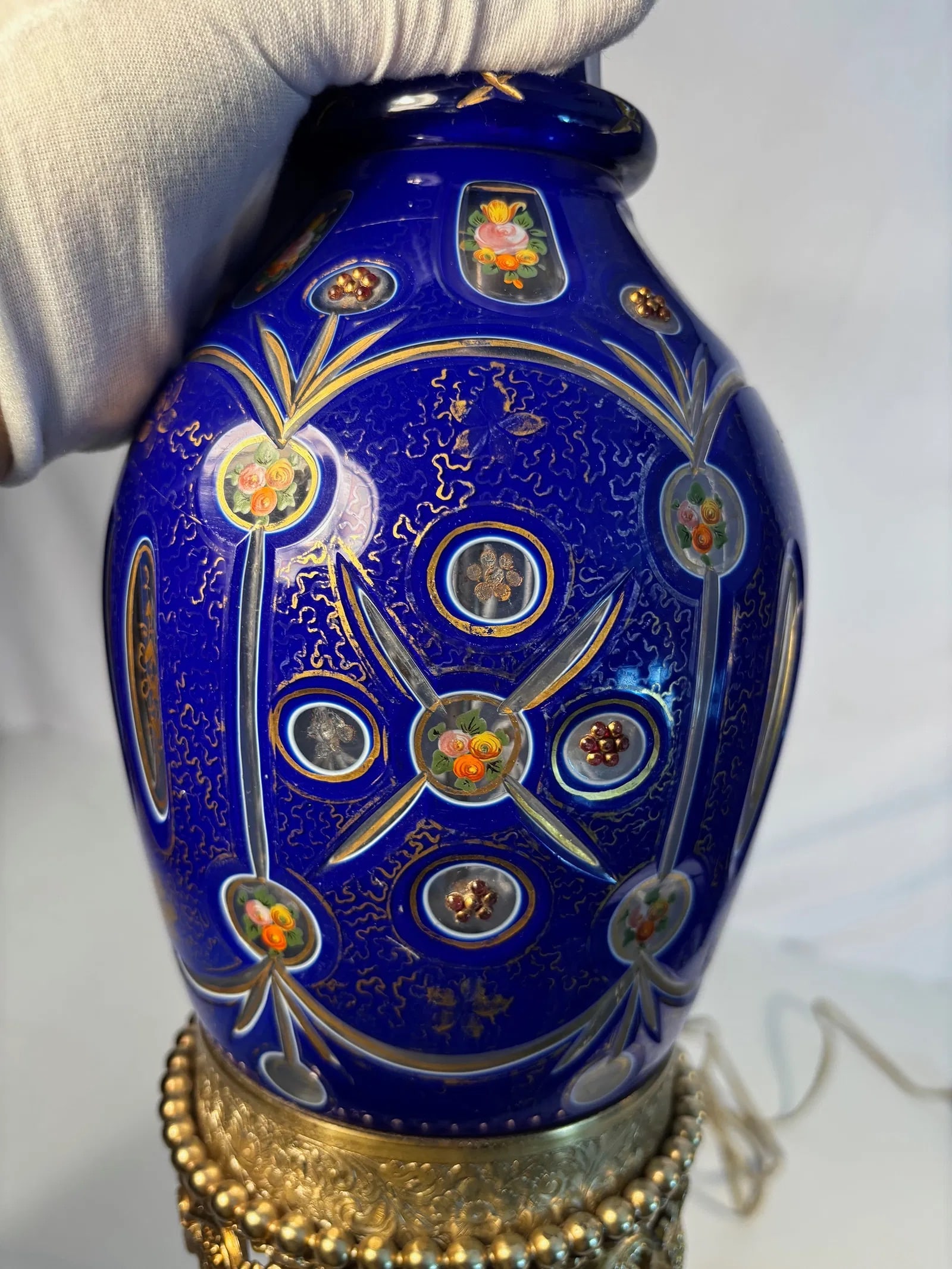A Bohemian Style Cobalt Blue Enameled and Gilt Glass Vase Mounted as a Lamp: A cobalt blue glass vase richly decorated with raised gilt scrollwork and polychrome enamel floral roundels, mounted in ornate gilt-metal ormolu base with figural masks and paw feet. Converted into a 