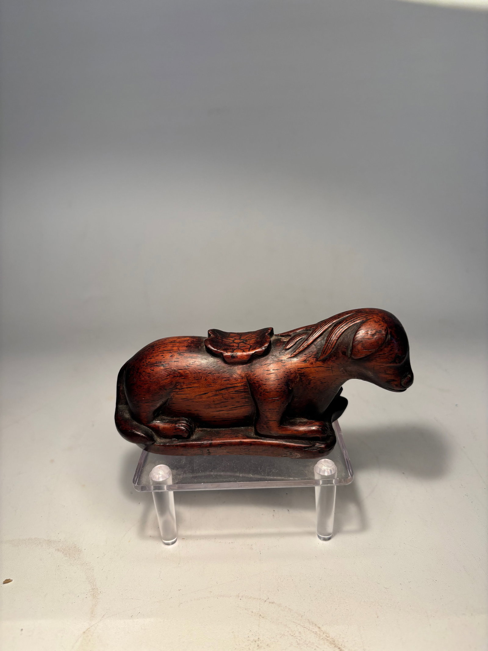 A Chinese rosewood/ huanghuali Carving – Reclining Horse: A finely carved Chinese hardwood figure of a reclining horse with a small monkey on its back. Carved from richly patinated reddish-brown wood, the figure is modeled in the round with a serene pose