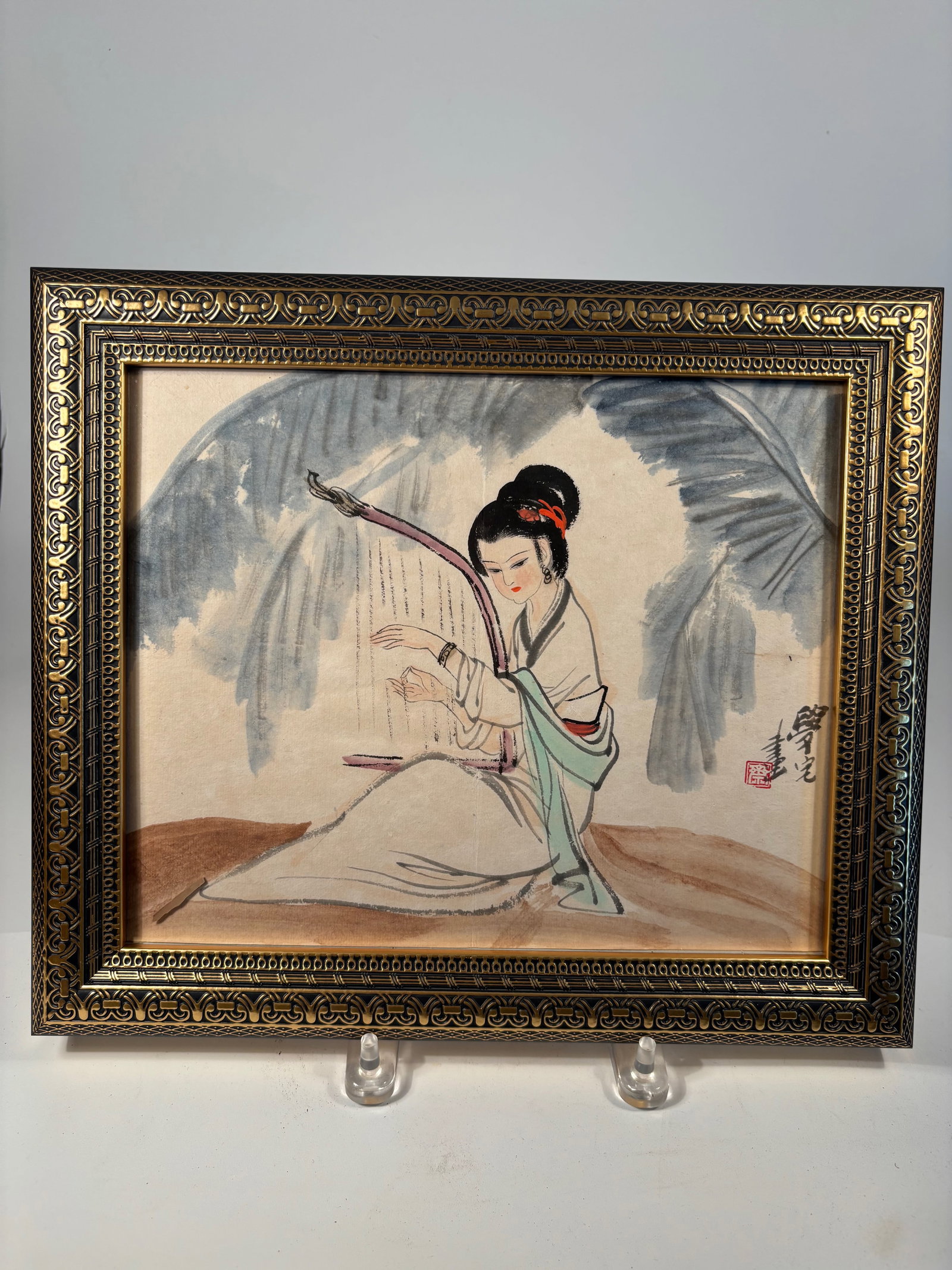A Chinese Watercolor Painting signed by artist: A finely executed Chinese watercolor painting on paper, depicting a graceful lady seated beneath broad foliage, delicately playing instrument. The composition showcases elegant brushwork and subtle us