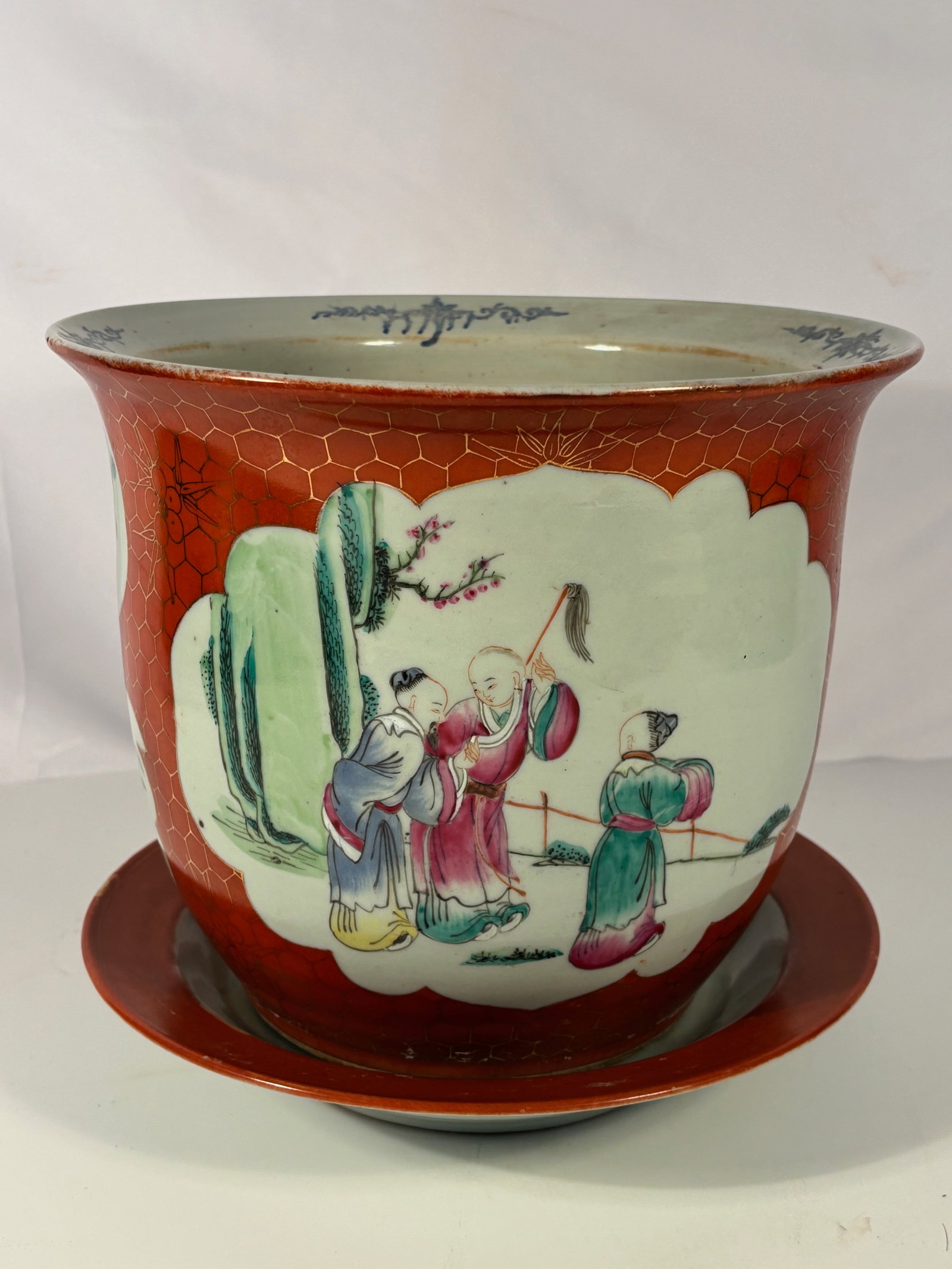 A Chinese Famille Rose Planter with Plate, Iron-Red and Gilt Honeycomb Ground, ‘CHINA’ Mark: Qing dynasty(1644-1912); Chinese famille rose porcelain planter with matching stand, the flared body decorated on an iron-red ground with gilt honeycomb pattern and shaped reserves enclosing figural a