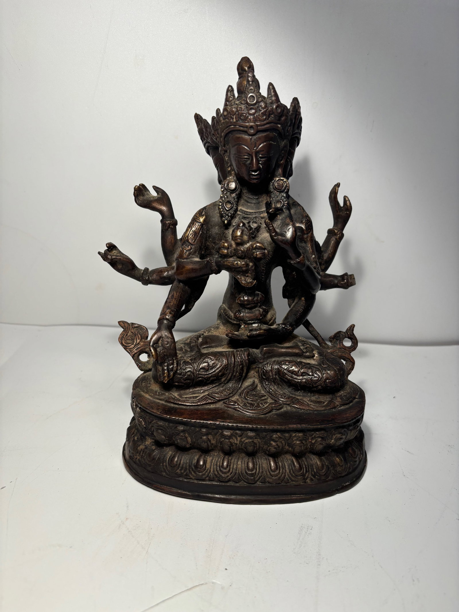 A Tibetan Bronze figure statue: Late 19th century , It features multiple arms and faces Seated on a lotus pedestal, with engraved decorations. Dimensions?Height: 7.25 inches.