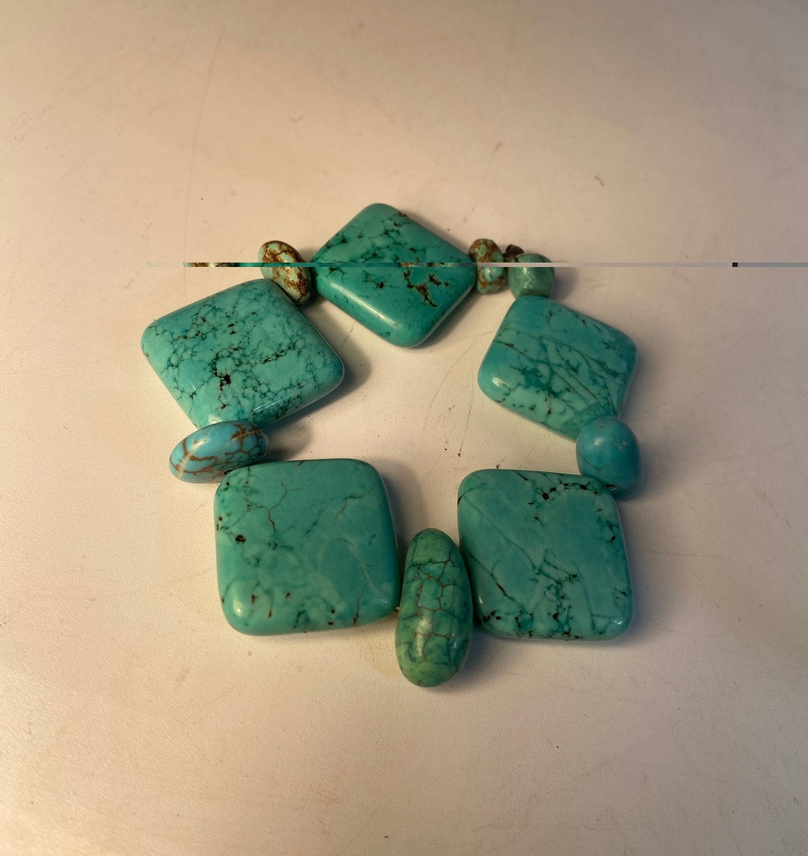 Turquoise Style Stone Stretch Bracelet: Bracelet composed of polished turquoise style stone beads in varied geometric forms with naturalistic matrix veining. Elastic stretch construction. Square beads approximately 1” x 1”.