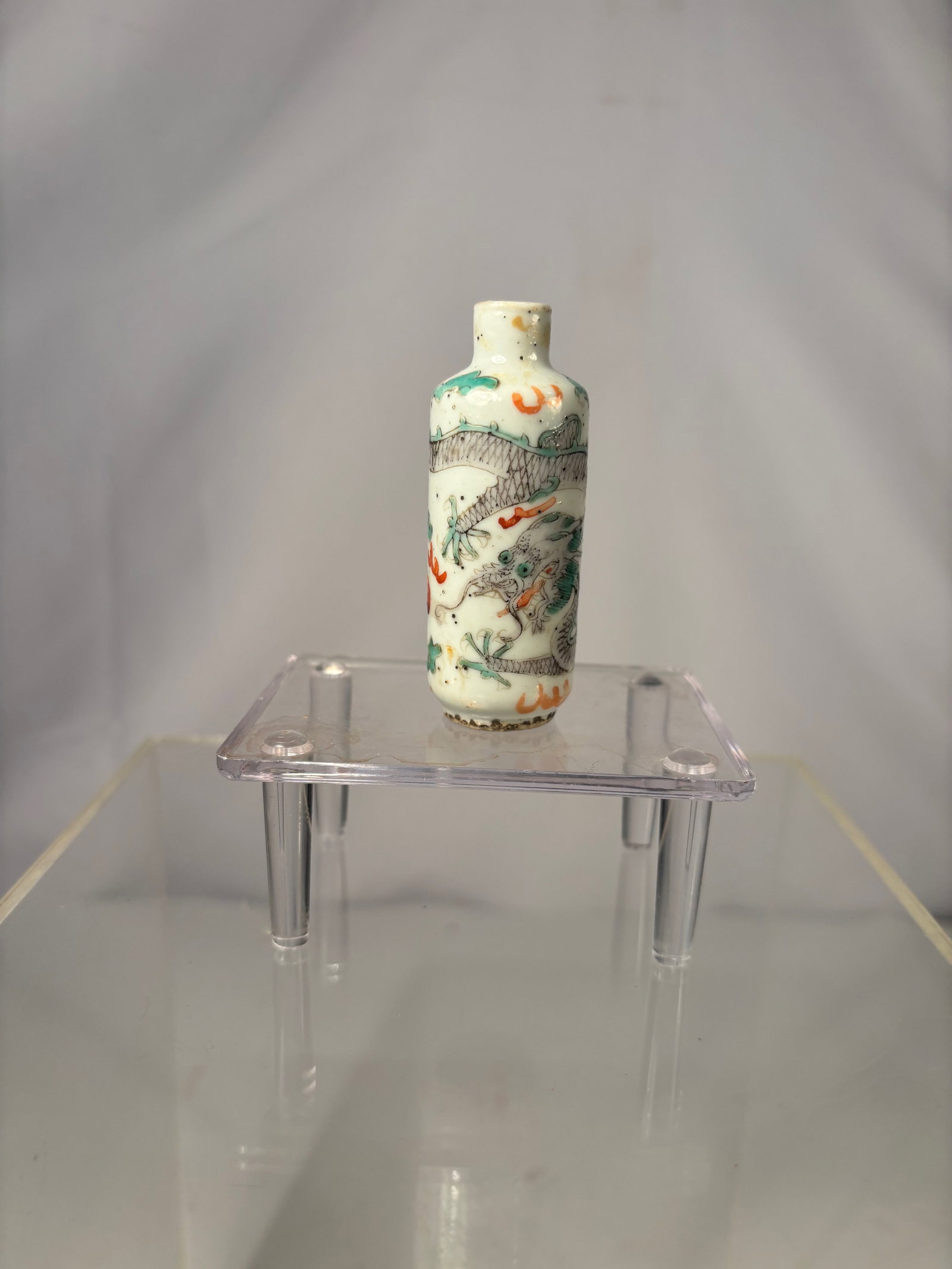 A Chinese Porcelain Snuff Bottle with Dragon and Landscape Decoration: Qing Dynasty(1644-1912) ; Porcelain snuff bottle of cylindrical form, decorated in underglaze blue and overglaze iron red and green enamels. The body is painted with a dragon amid clouds and a landsca