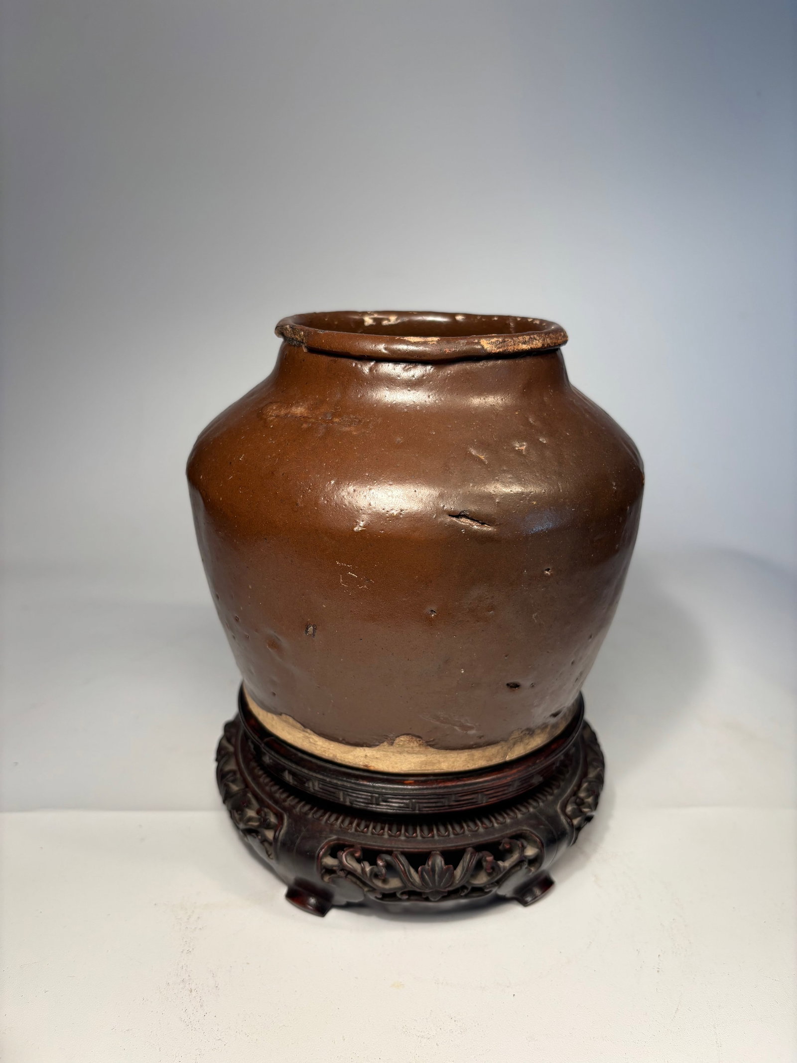 A Chinese Brown Glazed Ceramic Jar: Qing Dynasty(1644-1912); featuring a thick body with a rounded shoulder and short neck. The jar is covered in a rich, dark brown glaze with natural pitting and firing irregularities, characteristic of