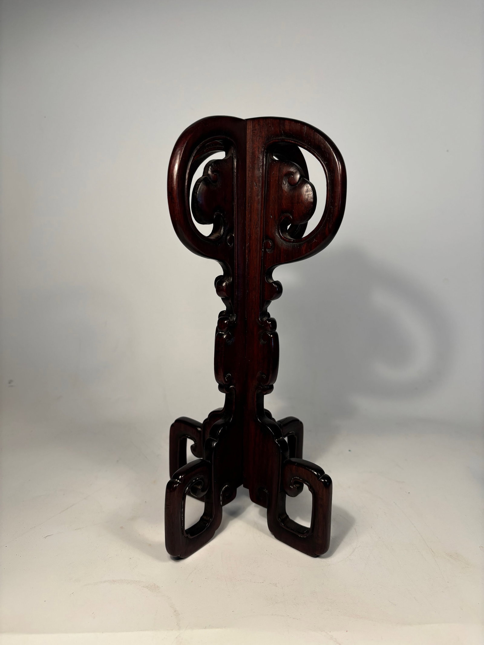 A Chinese Carved Rosewood Hat Stand: Crafted from richly grained rosewood with a deep reddish-brown tone, the piece features an elaborate interlocking structure with fluid scrollwork and pierced openwork throughout. The stand is