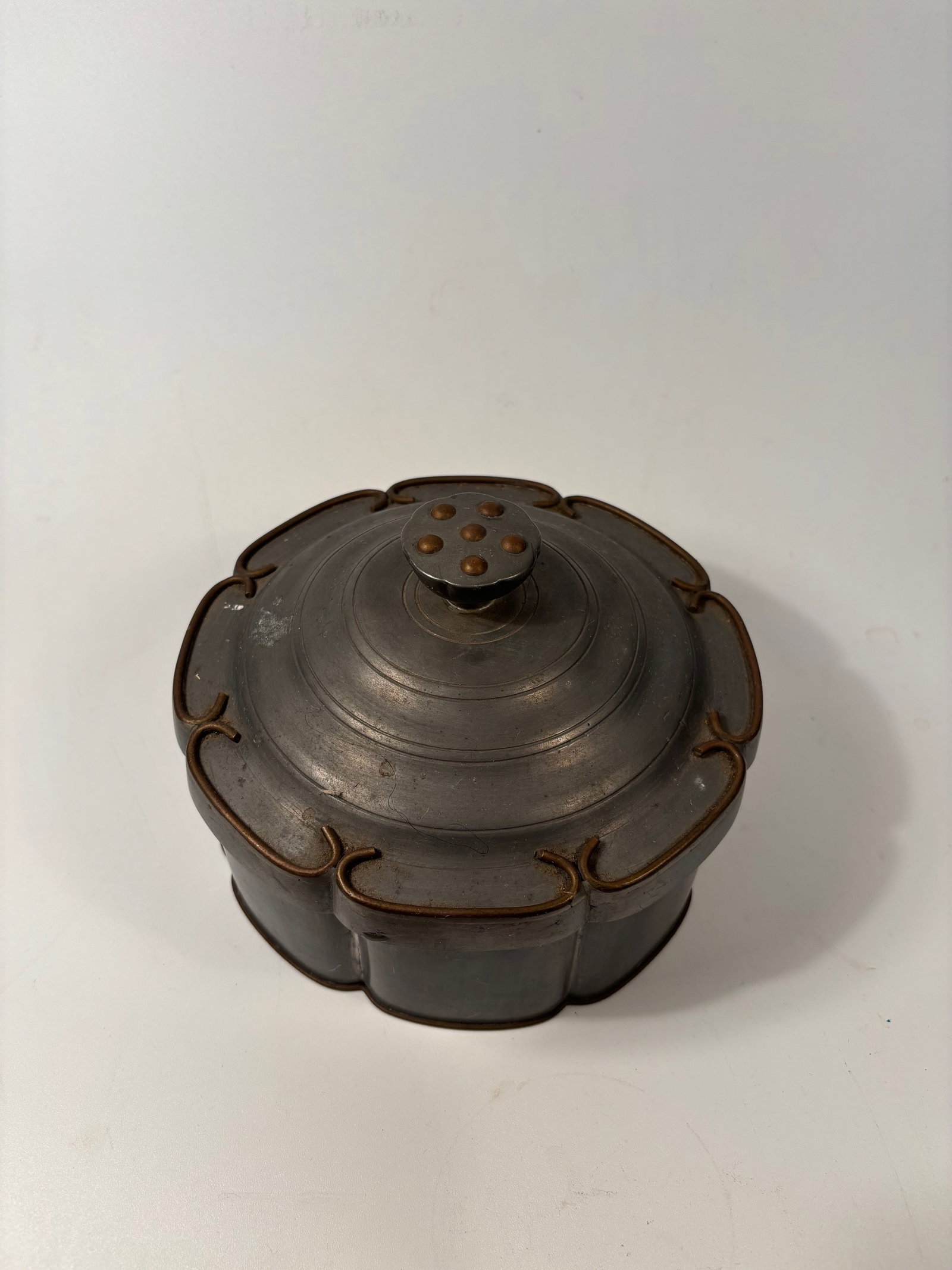 A Chinese pewter(mixed metal) liddedbox.: Qing dynasty(1644-1912); Primarily pewter possibly with inlaid copper or brass details.The lobed (petal-shaped) form is inspired by plum blossom or melon sections—often seen in scholar’s objects o