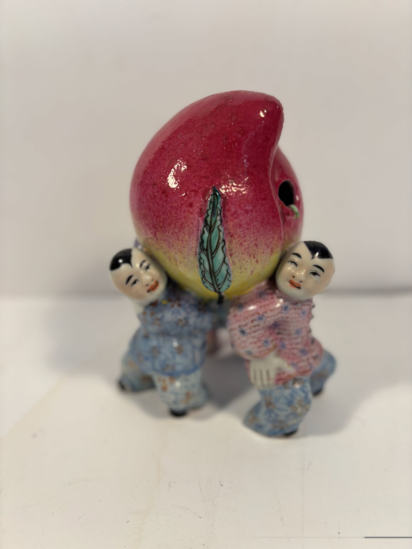 A Chinese famille rose Porcelain Figurine: 19th century; A beautifully crafted Famille Rose porcelain figurine depicting three boys joyfully holding a peach. Dimensions?HEIGHT: 8 inches; Width: 6 inches; Depth: 5 inches.