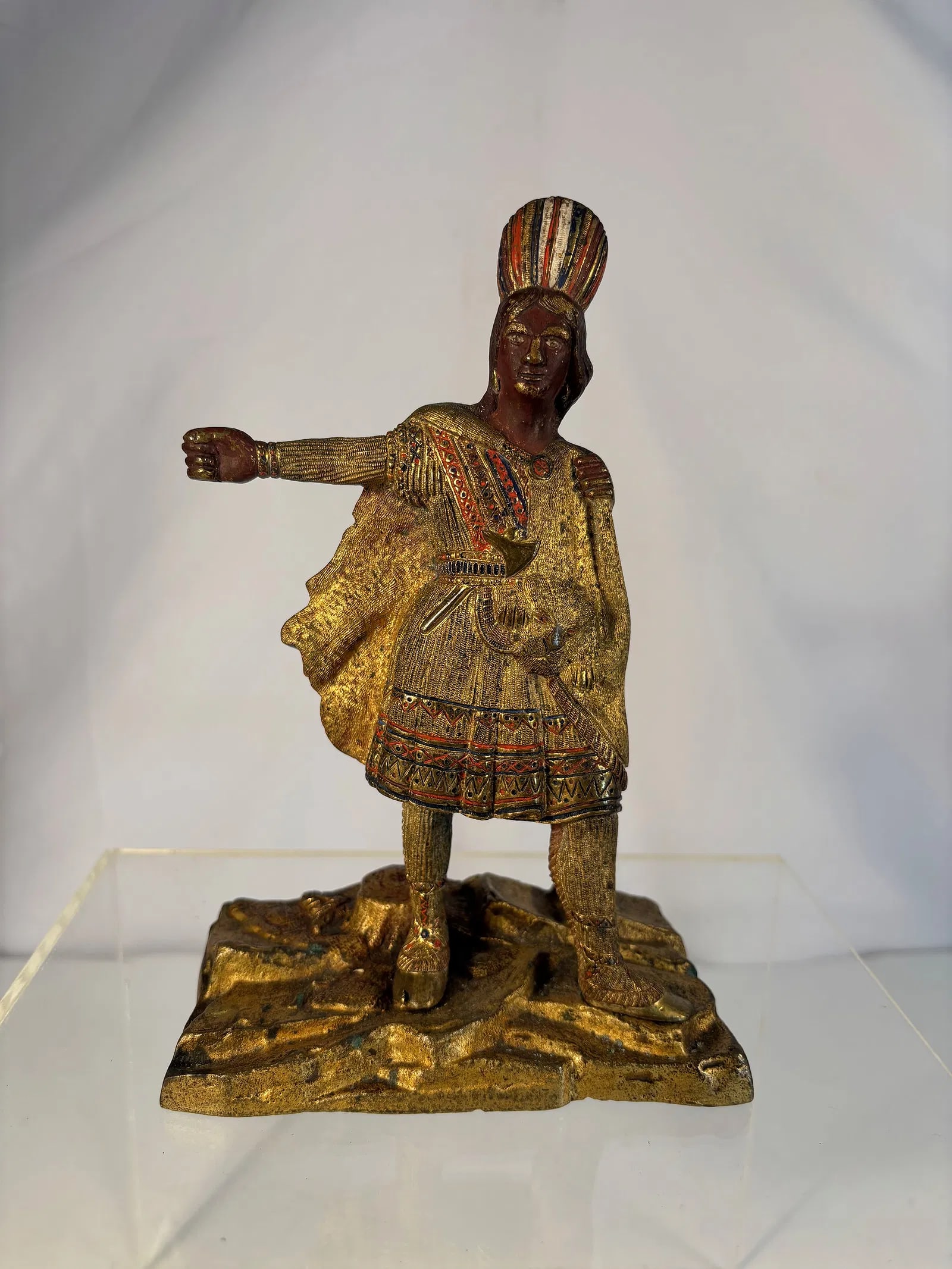 Finely Detailed Gilt and Painted Bronze Figure Depicting a “Cigar Store Indian,?? circa 1900: Finely cast and richly detailed figure of a Native American man in traditional dress, depicted standing with one arm extended and wearing a feathered headdress, patterned tunic, and moccasin-style