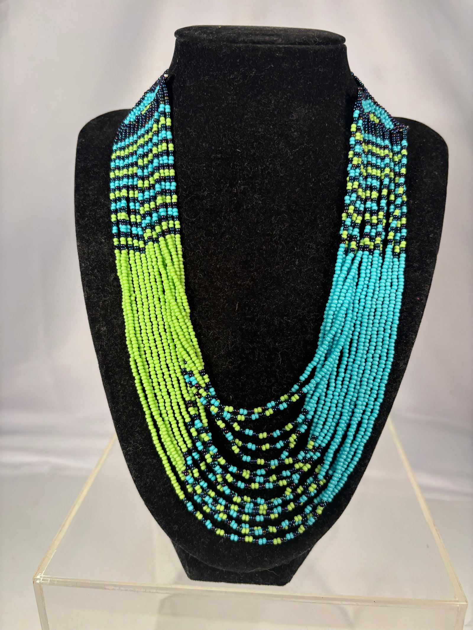 Native American Style Beaded Fringe Necklace: Handcrafted Native American style beaded necklace featuring turquoise-blue, black, and lime-green seed beads arranged in geometric patterns. The necklace is adorned with long beaded fringe drops and m