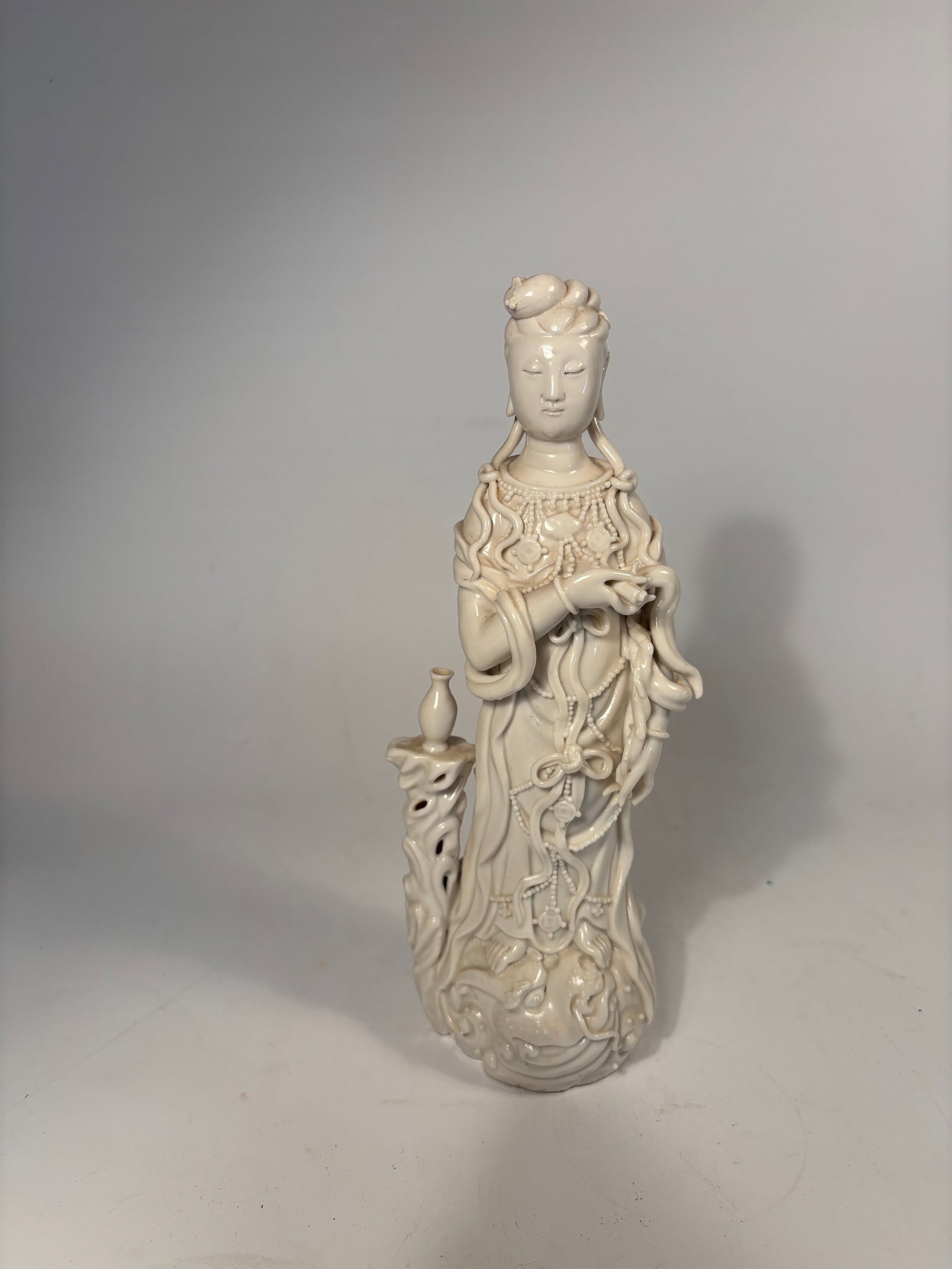 A Chinese Blanc de Chine Porcelain Guanyin Figure: 19th century; A finely crafted porcelain figure of Guanyin, the Buddhist bodhisattva of compassion, rendered in the elegant Blanc de Chine (Dehua) style. Standing gracefully, Guanyin holds a small ves
