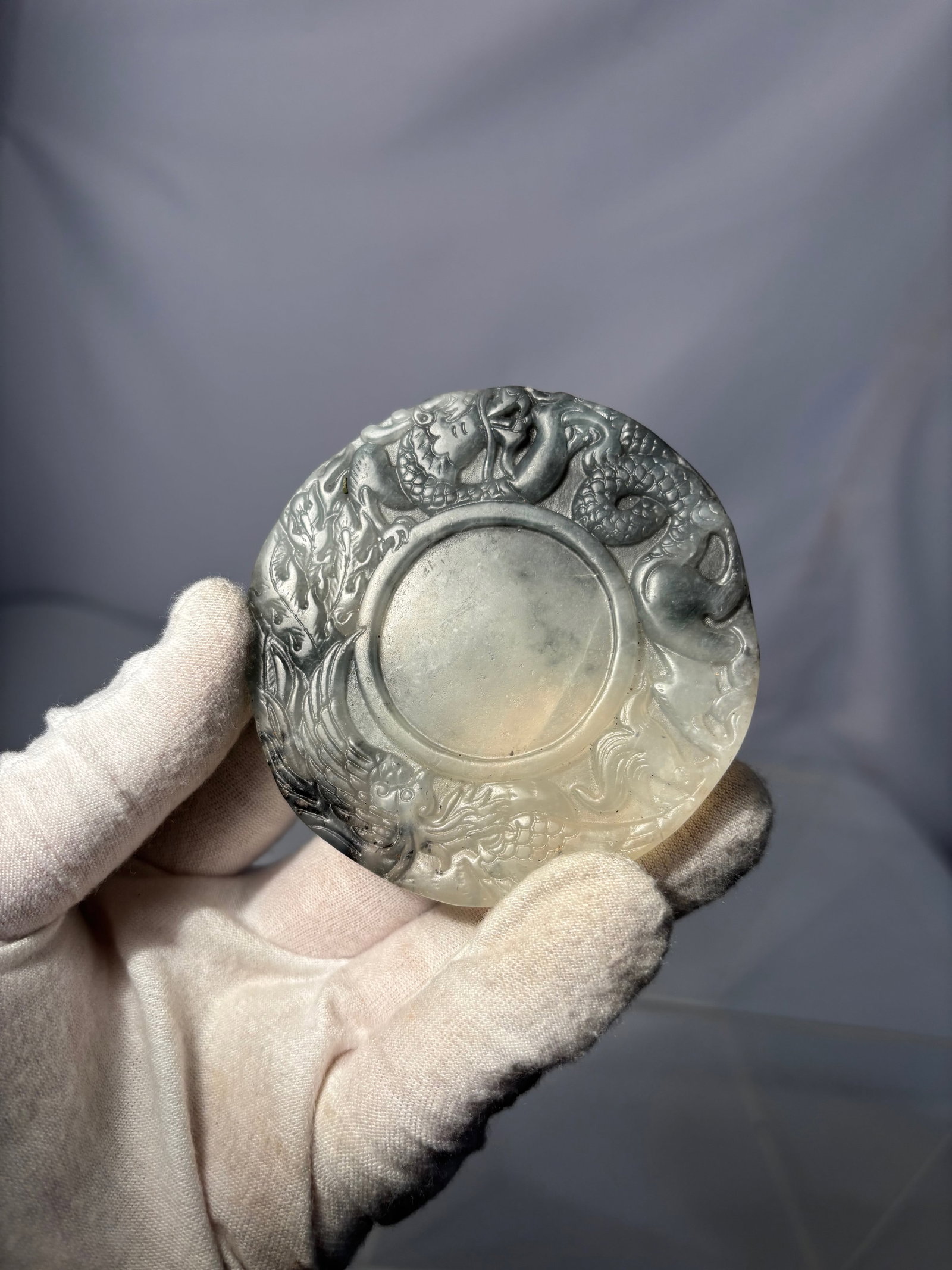 A Carved Black and White Jade Pendant with Dragon Motif: Round black-and-white jade carving featuring multiple dragons in high relief surrounding a central medallion. The stone displays natural contrasting tones with flowing dark and light coloration. Well 