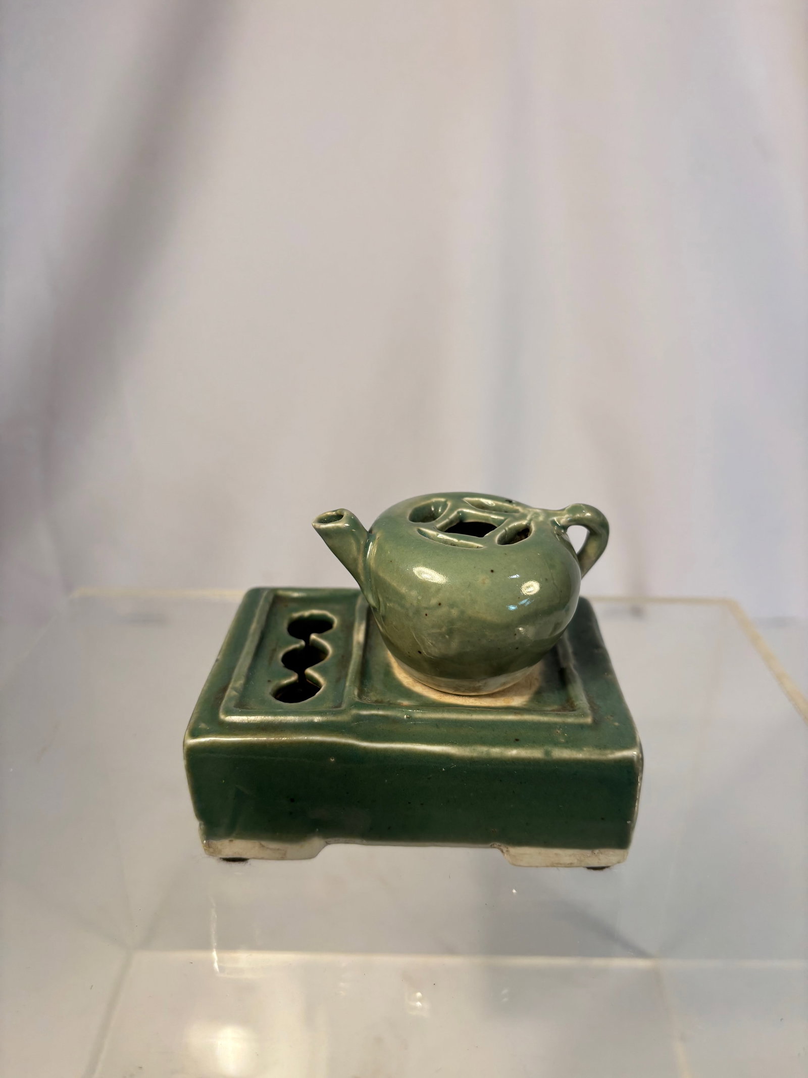 A Chinese Longquan-Style Celadon Water Dropper with Matching Stand, Qing Dynasty (1644-1912): A finely potted Longquan-style celadon water dropper, of compressed globular form with twin loop handles and a short spout, surmounted by a pierced domed cover for controlled pouring. The dropper rest