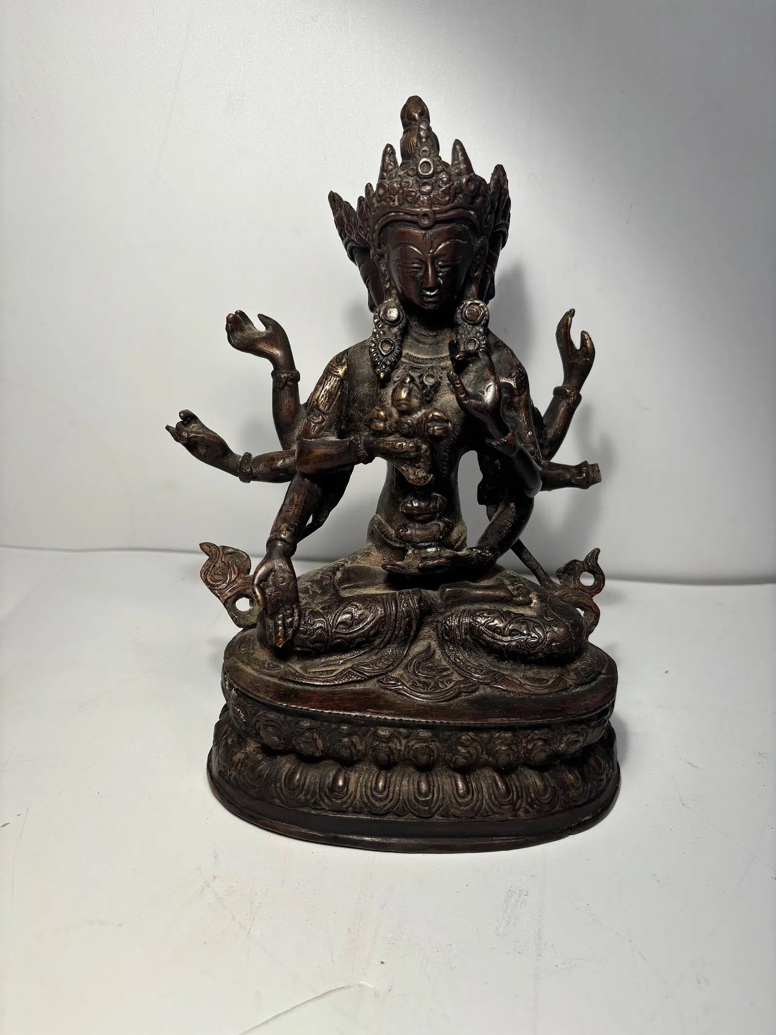 A Tibetan Bronze figure statue: Late 19th century , It features multiple arms and faces Seated on a lotus pedestal, with engraved decorations. Dimensions?Height: 7.25 inches.