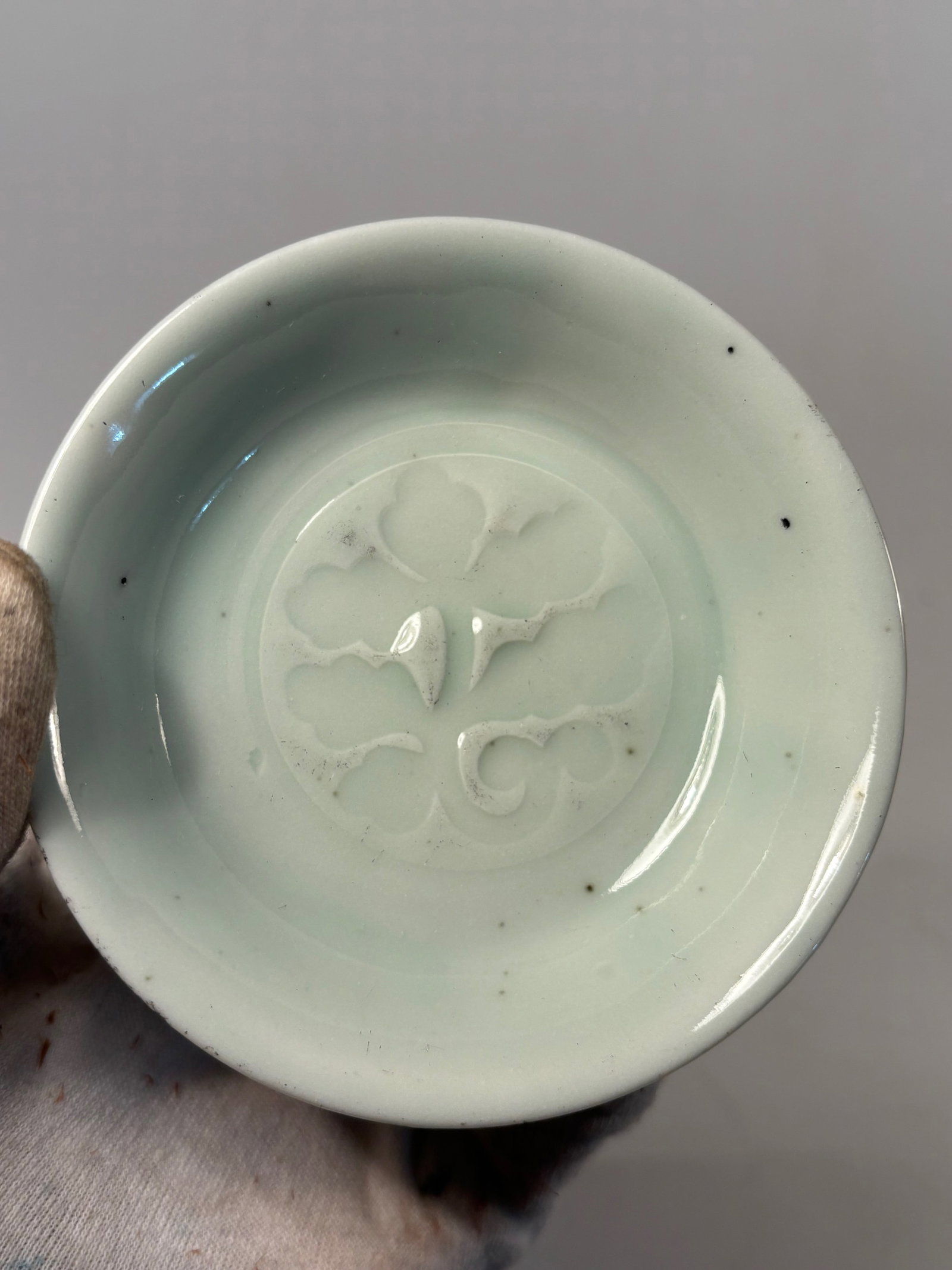 A Chinese celadon-glazed dish with MARK 'WAN LI NIAN ZHI': Qing dynasty(1644-1912); Chinese celadon-glazed porcelain dish featuring an impressed floral design at the center, covered with a soft green translucent glaze in the Longquan tradition with MARK 'WAN 