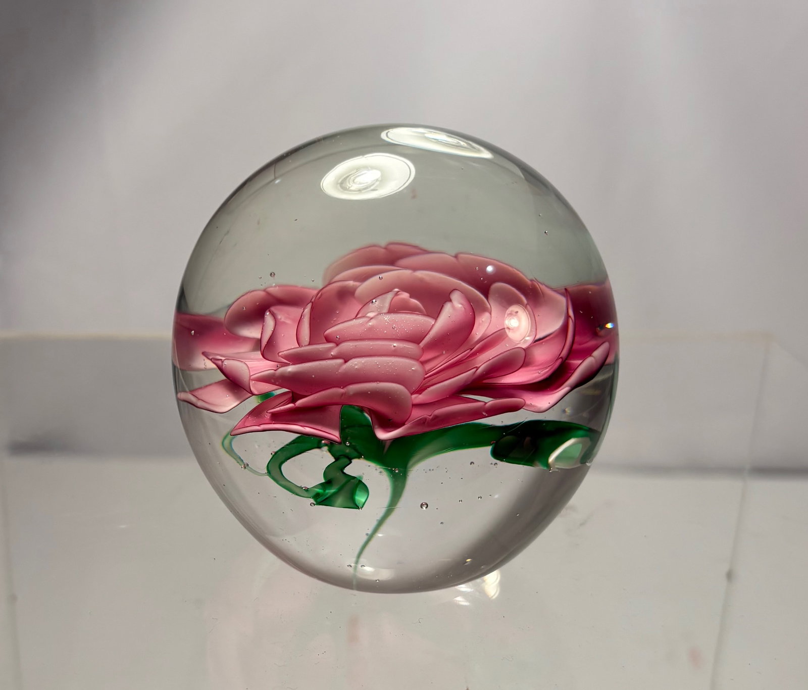 Art Glass Paperweight with Pink Rose Floral Motif: Art glass paperweight featuring a finely detailed pink rose floral motif, encased beneath clear glass. The flower is well modeled with layered petals and subtle shading, creating good depth and visual