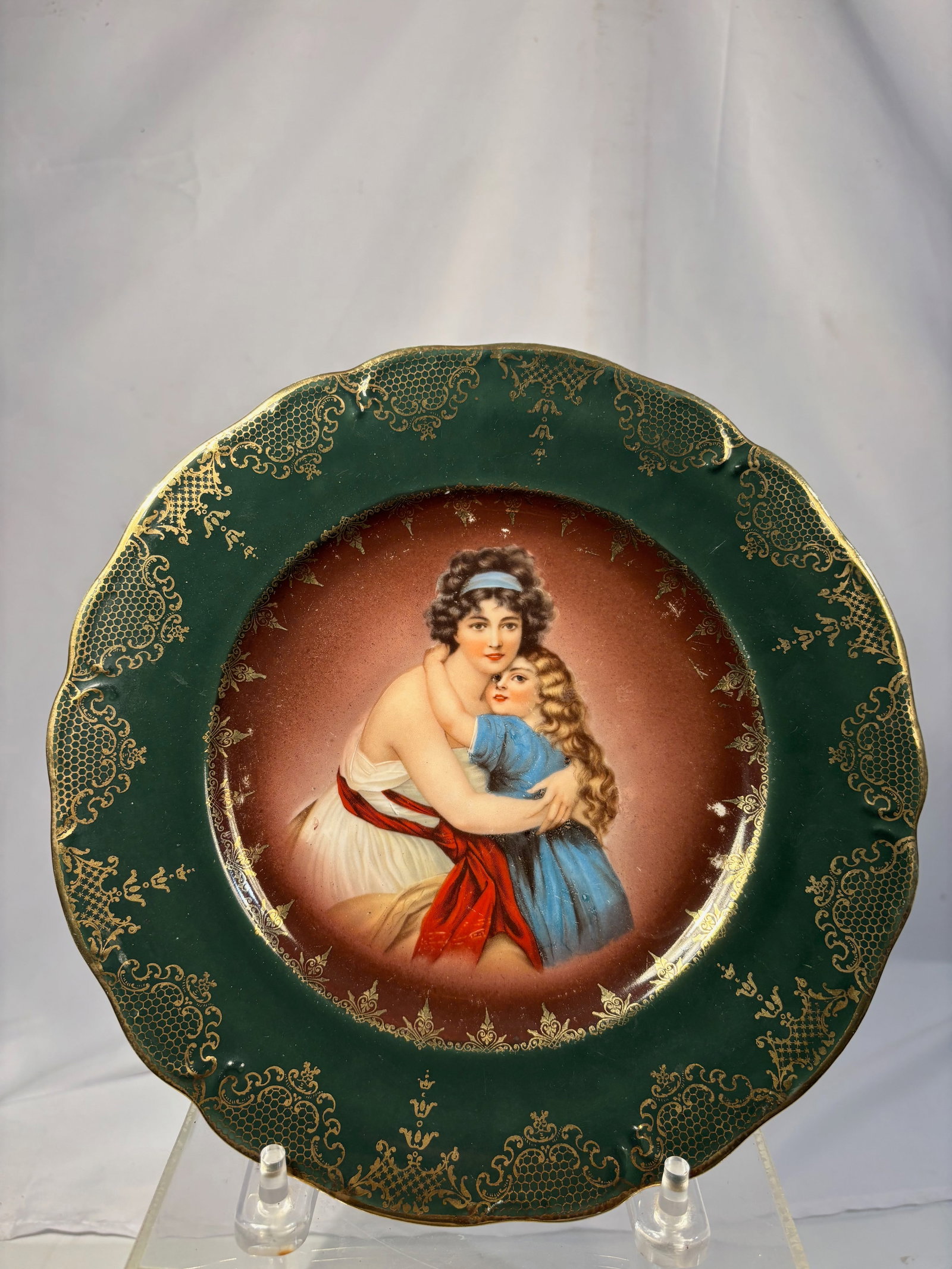 German Bavaria Portrait Porcelain Cabinet Plate: German porcelain cabinet plate featuring a romantic portrait of a mother embracing a young child at center, surrounded by a deep green border with gilt decoration. Bearing a crowned Bavaria-style mark