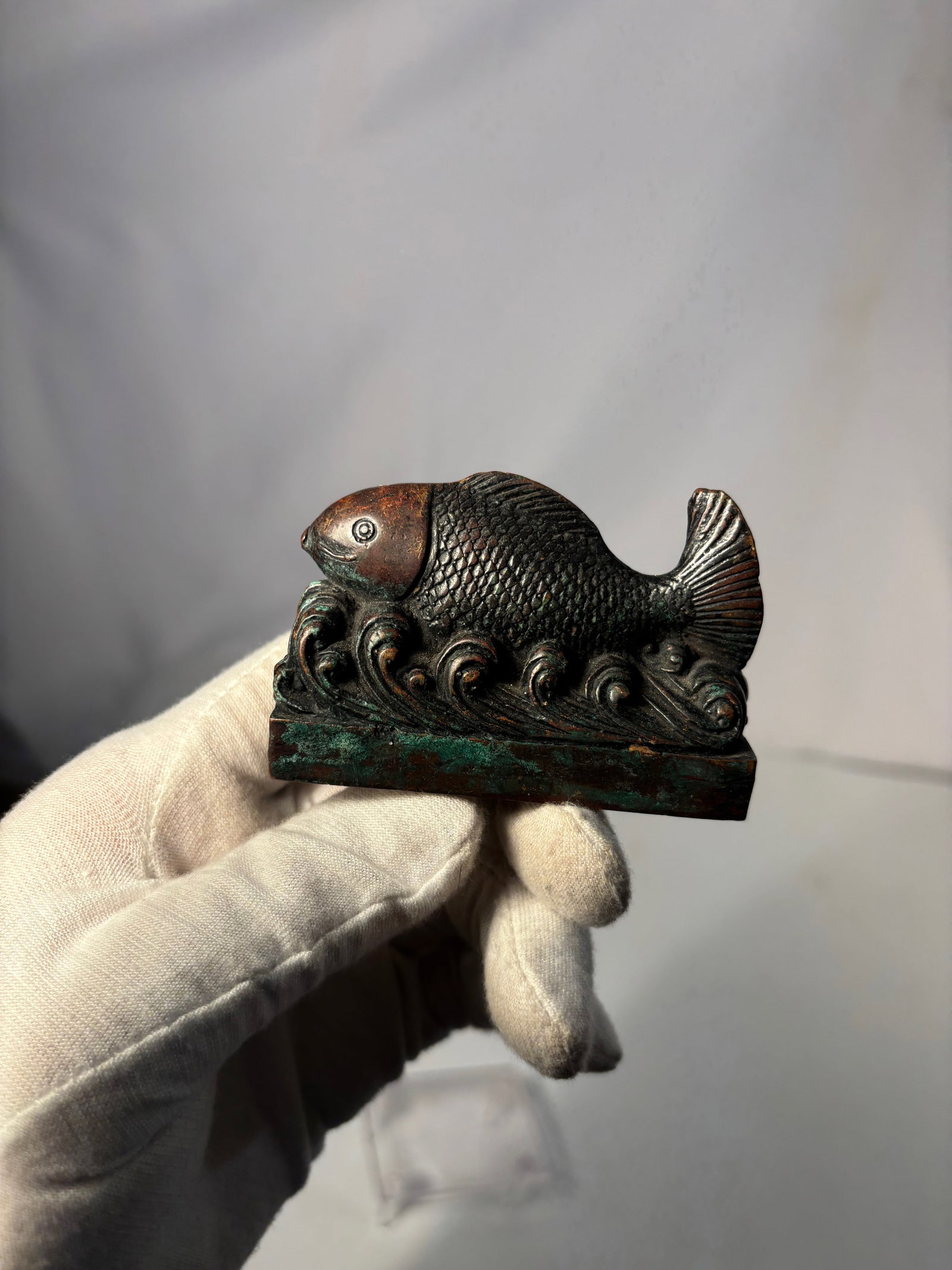 A Japanese Bronze Seal with Fish-and-Waves Finial Edo–Meiji Period: 18th-19th century; A Japanese bronze seal (hanko), Edo to Meiji period, surmounted by a sculptural finial in the form of a fish swimming amid stylized waves. Cast in bronze with a dark patinated surfa