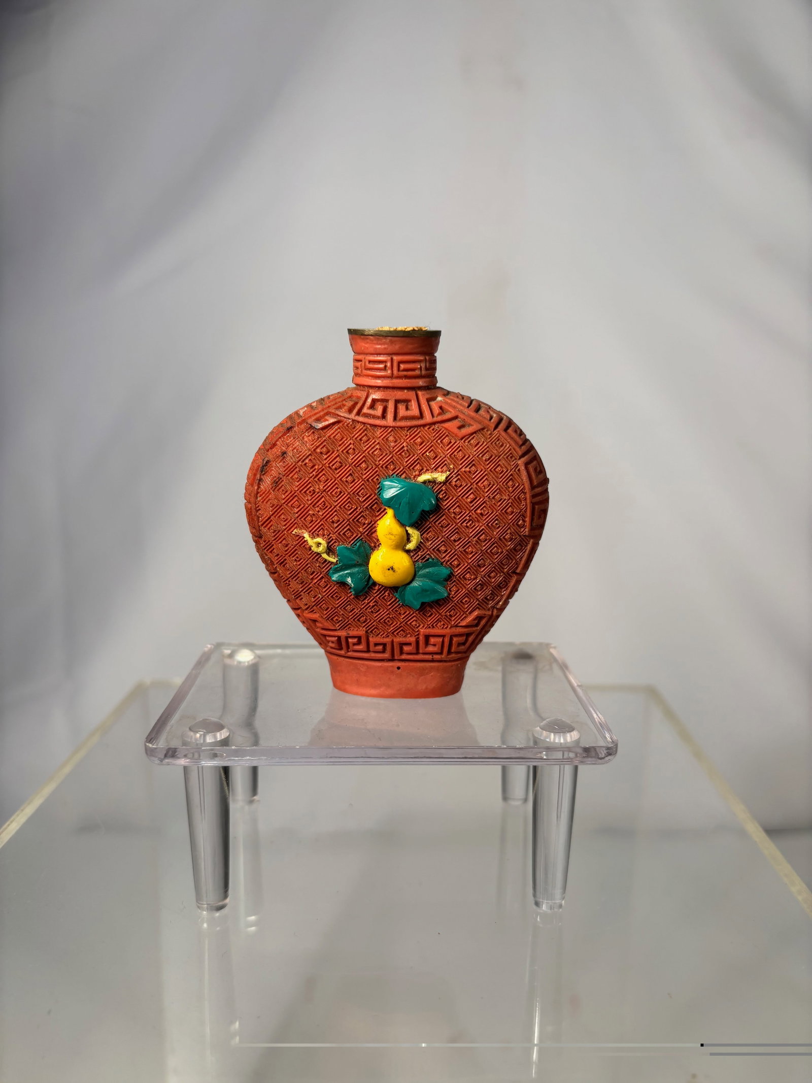 A Chinese Cinnabar-Style Snuff Bottle with Double Gourd Motif, 20th Century: Molded cinnabar-style snuff bottle of flattened ovoid form, decorated overall with a repeating leiwen (thunder) pattern and applied with a raised double gourd and leafy vine motif in contrasting color