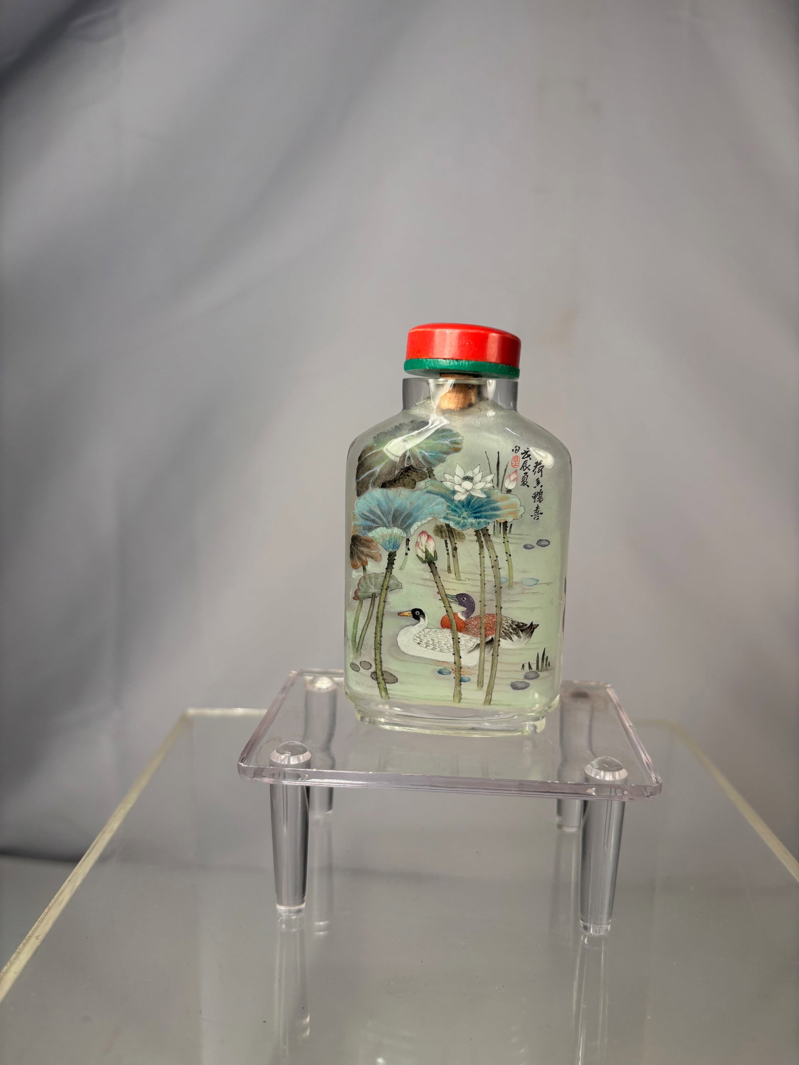A Chinese Inside-Painted Glass Snuff Bottle, by Liu Ziyi: A Chinese inside-painted glass snuff bottle depicting mandarin ducks beneath lotus plants, painted in fine detail with soft coloration. The interior is signed ???? (Liu Ziyi) and bears red seals. Fitt