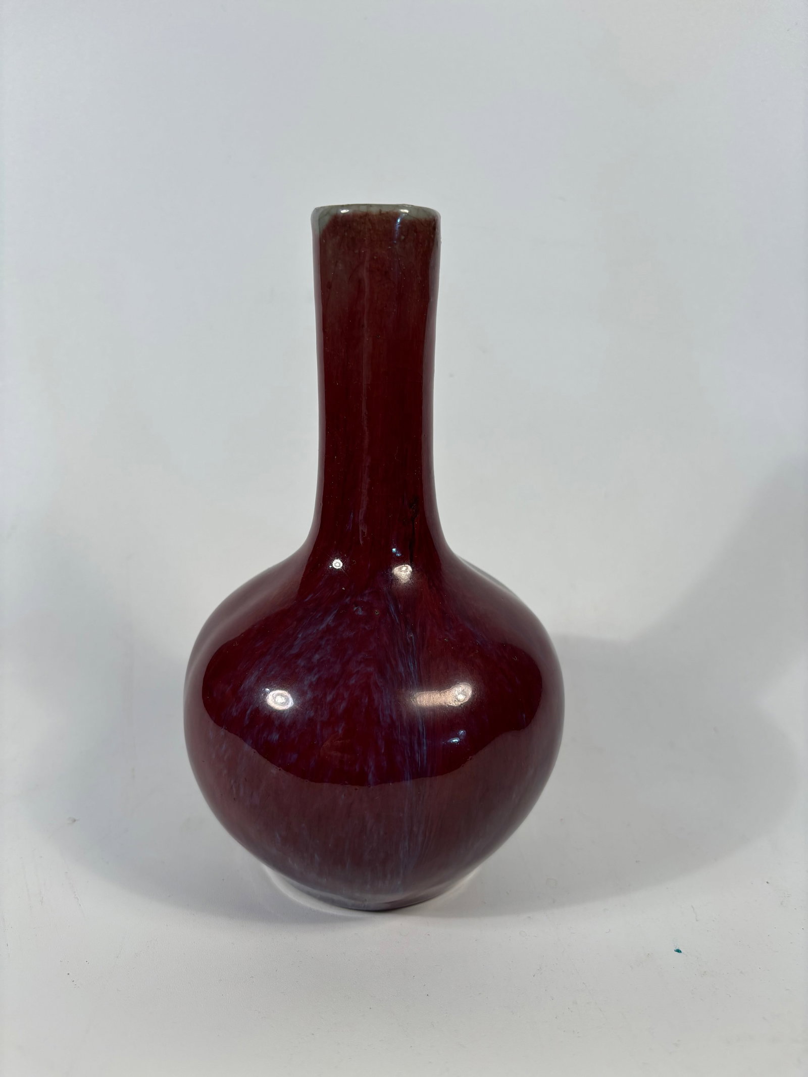 A Chinese flambé-glazed porcelain vase: Qing dynasty(1644-1912); The long neck and globular body is a classic yuhuchunping.The vibrant deep red with streaks of lavender, purple, and blue is characteristic of a flambé glaze (called “Junya