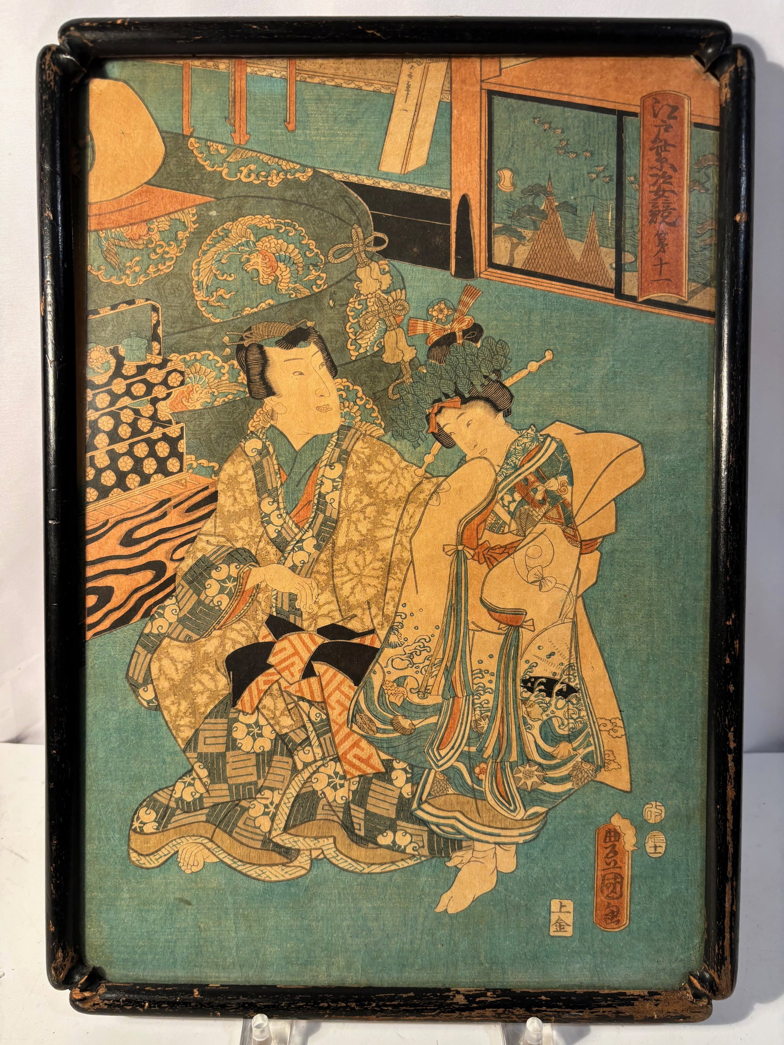 A Japanese Ukiyo-e Woodblock Print by Utagawa Toyokuni III (Kunisada), Interior Genre Scene, Late: A Japanese ukiyo-e polychrome woodblock print depicting an elegant interior genre scene with a finely dressed courtesan and male companion seated within a richly appointed room. The composition featur