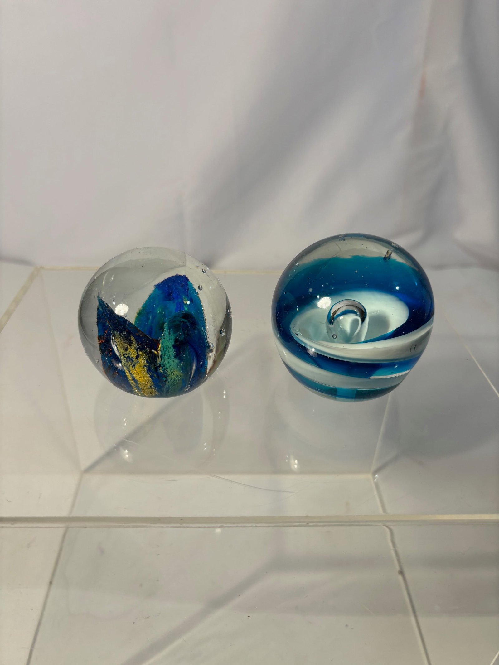 Two Art Glass Paperweights, Blue Swirl & Abstract Inclusion: Two contemporary studio art glass paperweights. One example of spherical form with internal abstract inclusion in blue, green, and amber tones suspended within clear glass. The second with layered blu