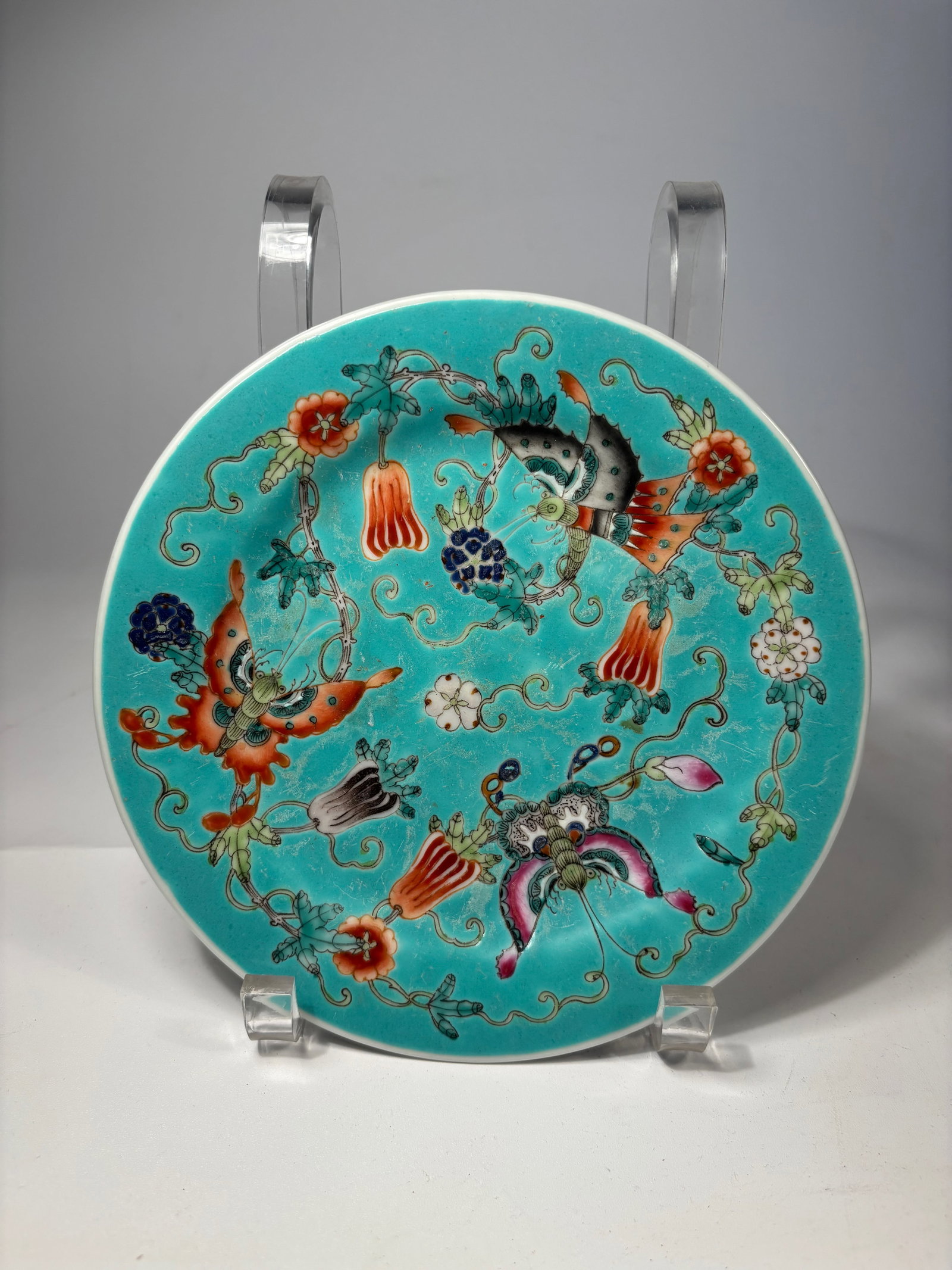 A Chinese famillie rose porcelain plate: A finely enameled Chinese porcelain plate decorated in the famille rose (fencai) palette on a vibrant turquoise ground. The central design features phoenixes, symbolic of beauty and renewal, surrounde