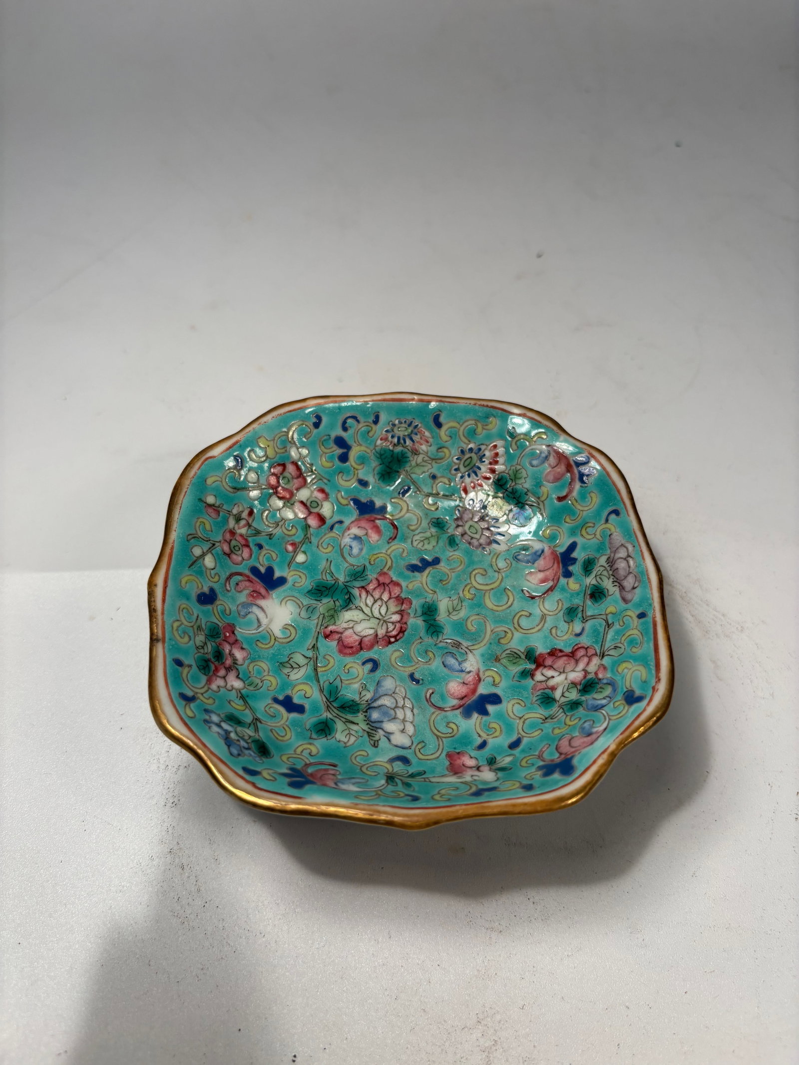 A Chinese famille rose porcelain footed dish with "TONGZHI" mark: QING DYNASTY(1644-1912); Of lobed form, the shallow dish raised on a short foot and enameled in famille rose palette over a turquoise ground with scattered flowers, butterflies, and foliage. The foot 
