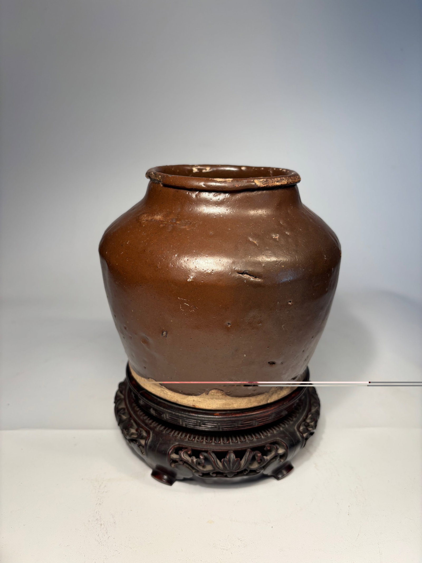 A Chinese Brown Glazed Ceramic Jar: Qing Dynasty(1644-1912); featuring a thick body with a rounded shoulder and short neck. The jar is covered in a rich, dark brown glaze with natural pitting and firing irregularities, characteristic of