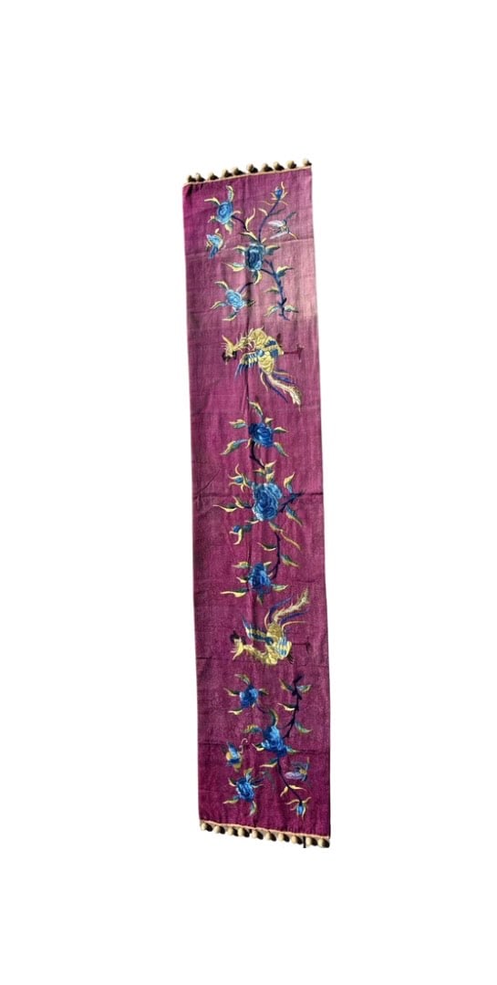 A Chinese silk embroidered panel: 19th century;The design includes phoenix-like birds and stylized blue peony flowers, embroidered on a rich purple or magenta silk; Dimensions?Length: 70 inches; Width: 14.5 inches.