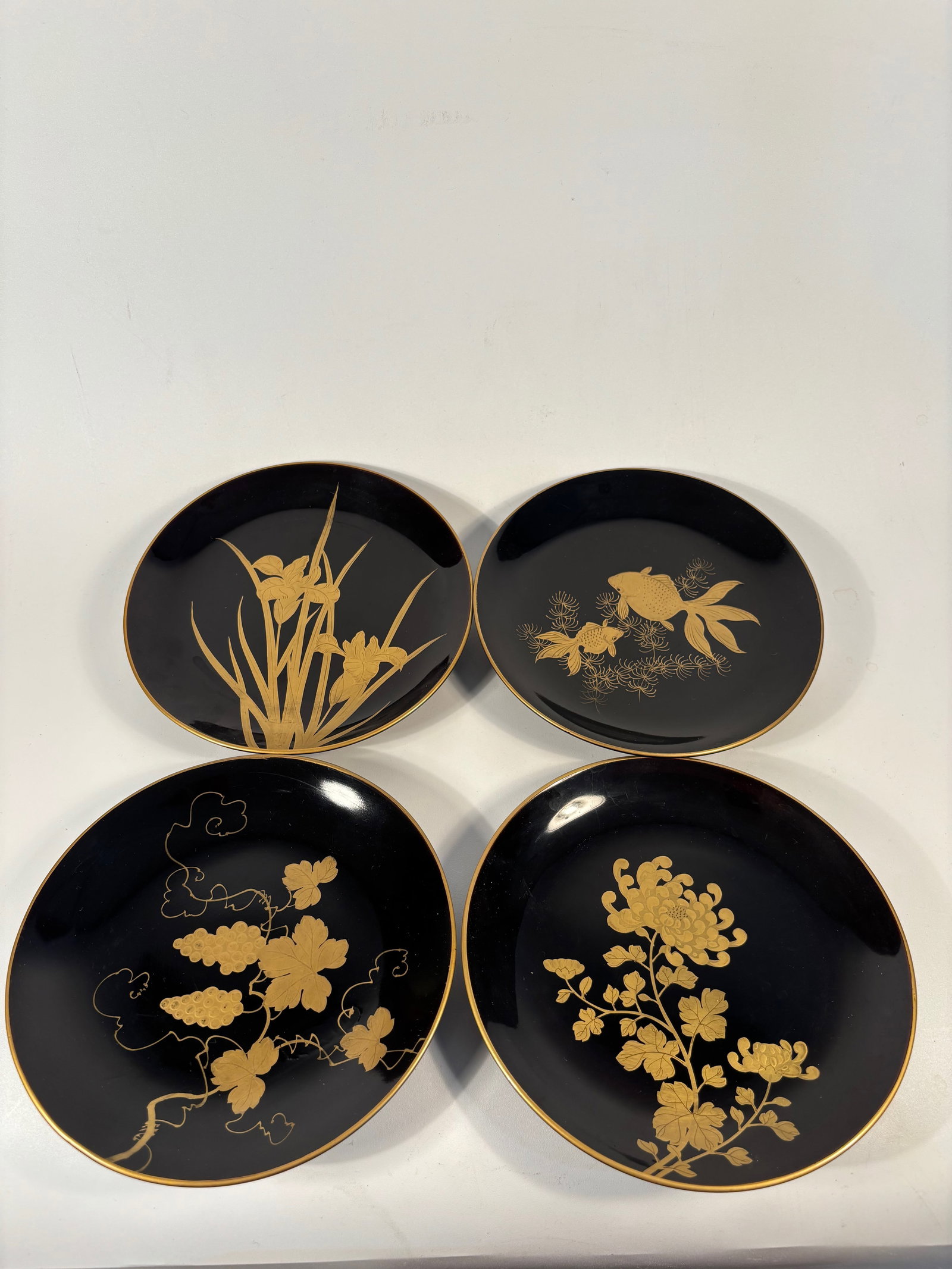 Set of 4 Japanese Makie Lacquer plates: Each plate finely decorated in gold maki-e on black lacquer with traditional Japanese motifs including plum blossoms, cranes in flight, butterflies, and flowering vines. The designs are delicately ren