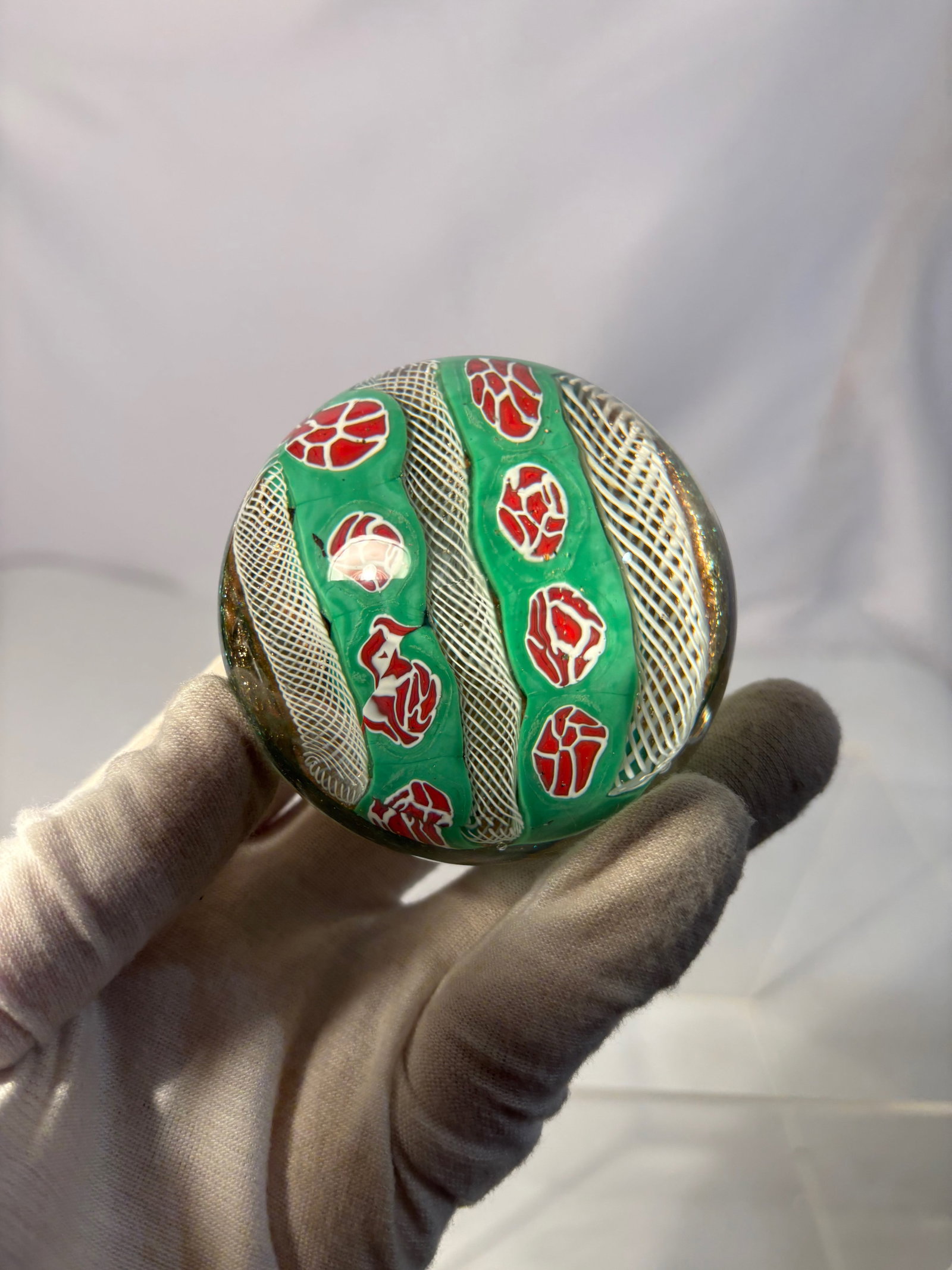 A Murano Glass Classic Millefiori Art Glass Paperweight, Italy: Decorative art glass paperweight by Murano Glass Classic, Italy. The rounded form features a colorful millefiori-style design composed of red, green, and white patterned elements arranged against a gr